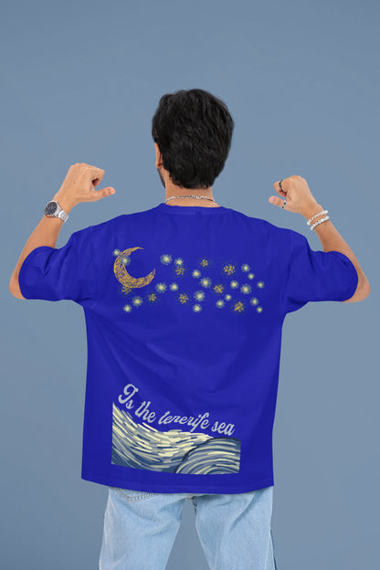 Back view of a male model wearing a royal blue oversized t-shirt featuring a beach at night with a starry sky above, inspired by Ed Sheeran's "Tenerife Sea."