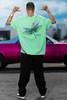 Back view of a male model wearing a mint green oversized t-shirt featuring a nature-inspired design with a blue dragonfly perched on flowers amidst green grass. Ideal for those who love springtime aesthetics and dragonfly imagery.