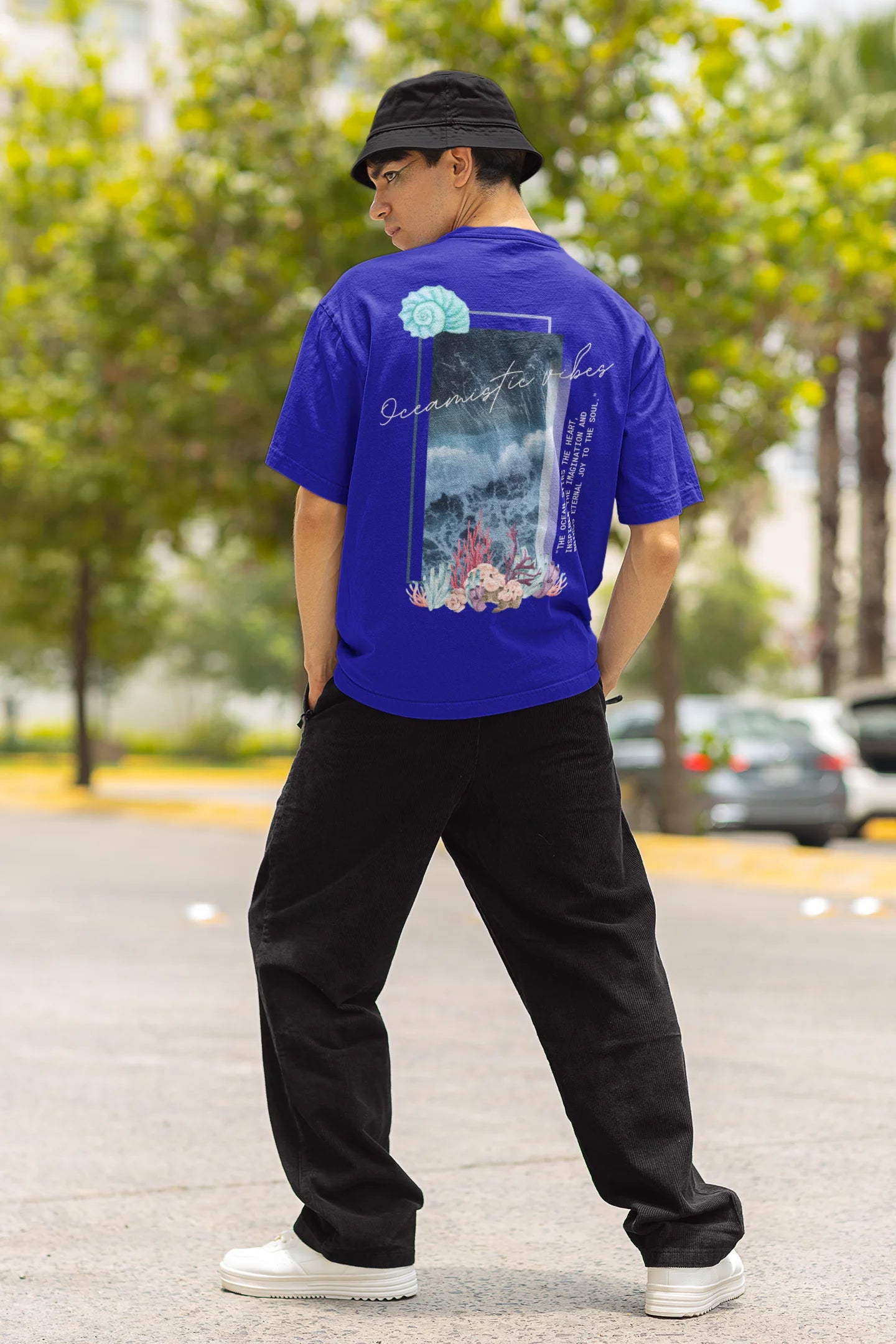 Back view of a male model wearing a royal blue Oversized t-shirt featuring a stunning design of corals and shells, evoking a serene underwater atmosphere.