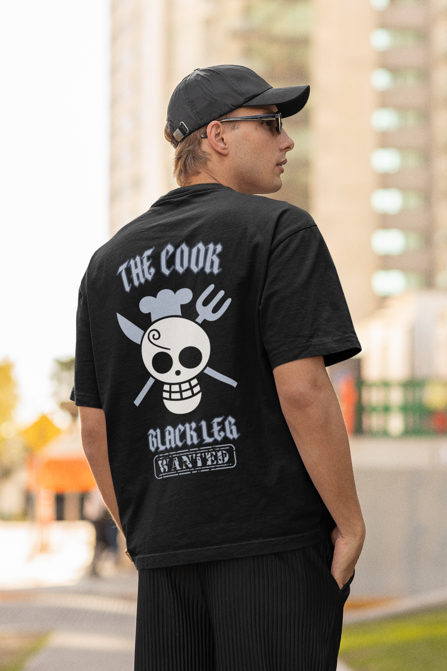 Back view of a male model wearing a black oversized t-shirt featuring Sanji's skull and crossbones logo and the text "The Cook and Black Leg."