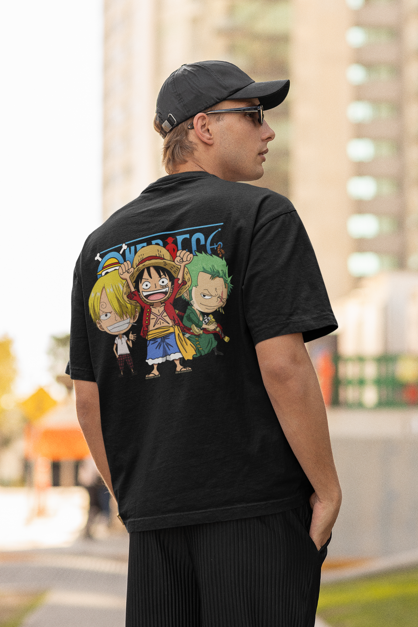 Back view of a male model wearing a black oversized t-shirt featuring chibi versions of the main characters from the One Piece anime.