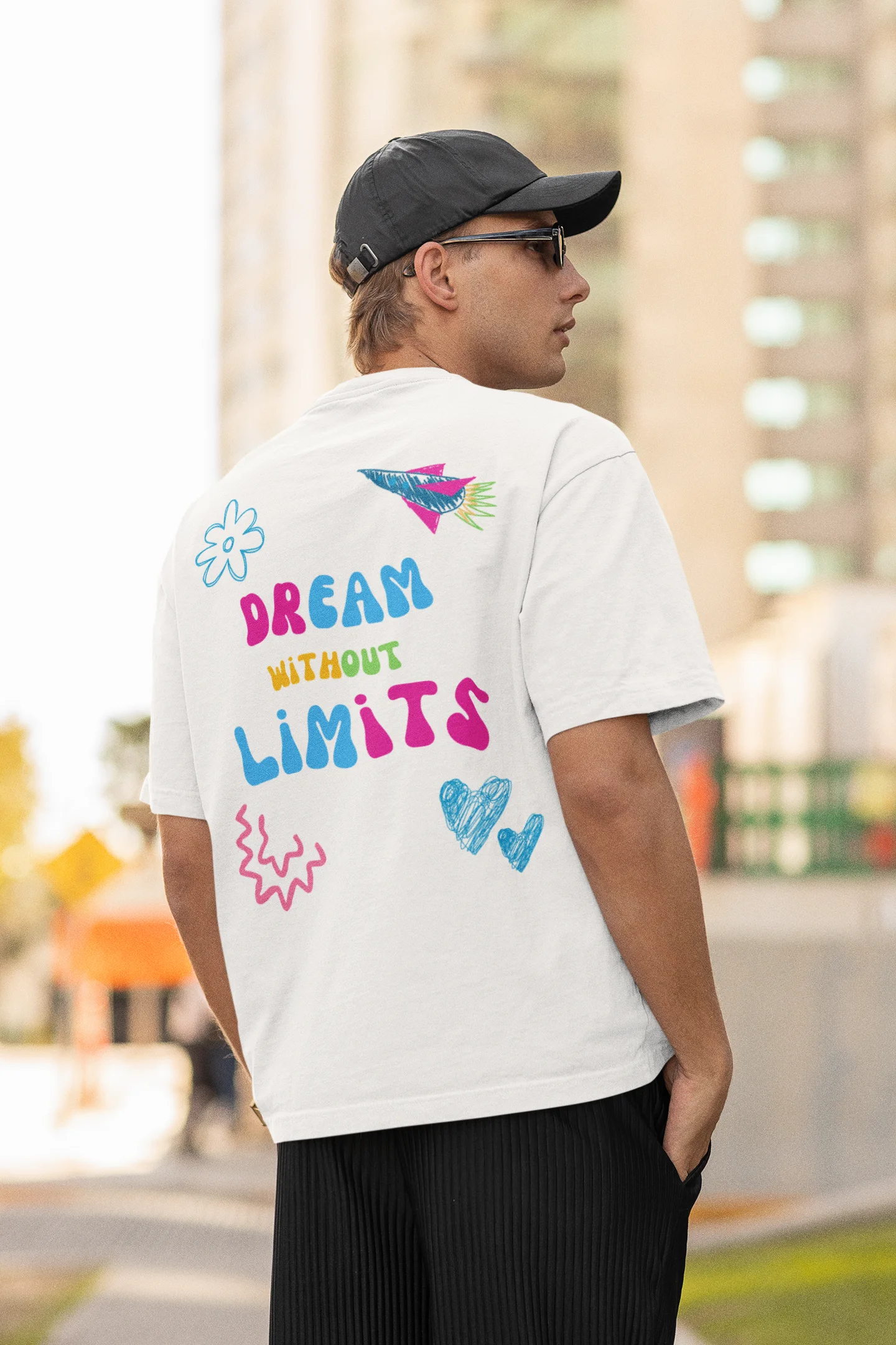 Back view of a male model wearing an off-white oversized t-shirt featuring colorful "Dream Without Limits" text, offering an inspiring and uplifting aesthetic.