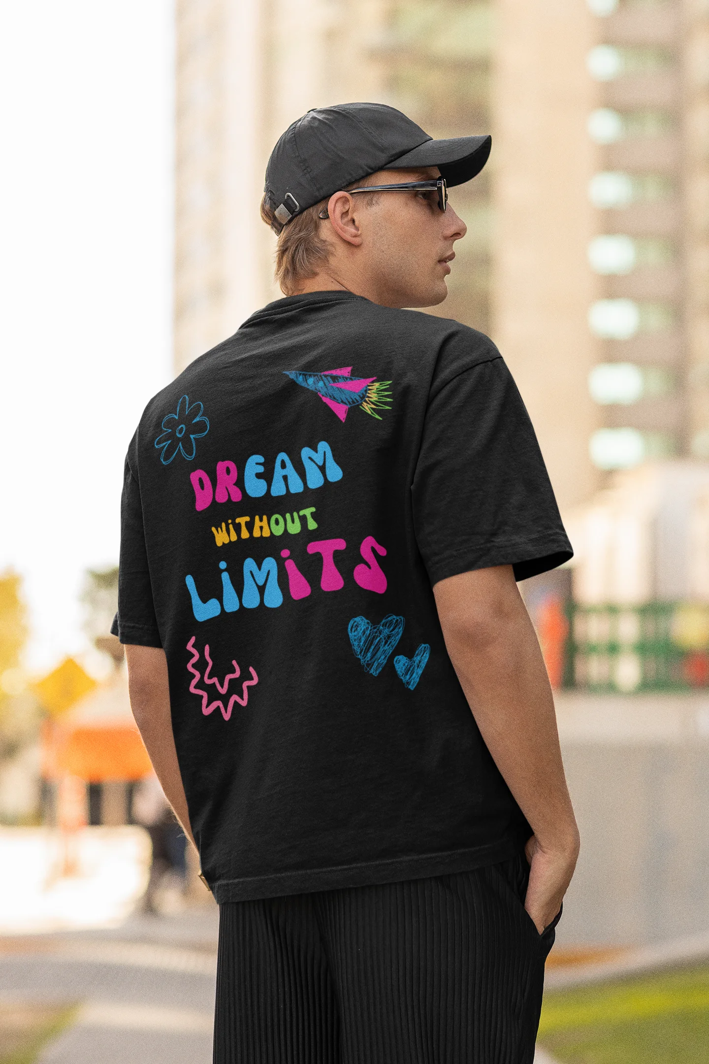Back view of a male model wearing an black oversized t-shirt featuring colorful "Dream Without Limits" text, offering an inspiring and uplifting aesthetic.