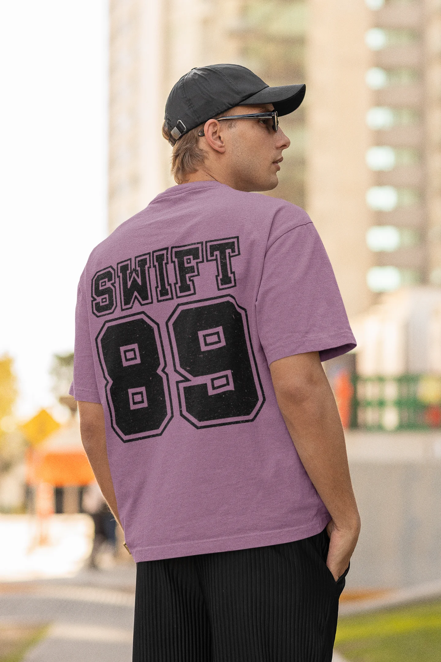 Back view of man wearing Dirty Purple coloured Oversize T-shirt featuring Taylor Swift 1989 design, Taylor's Version, and Eras Tour Merch