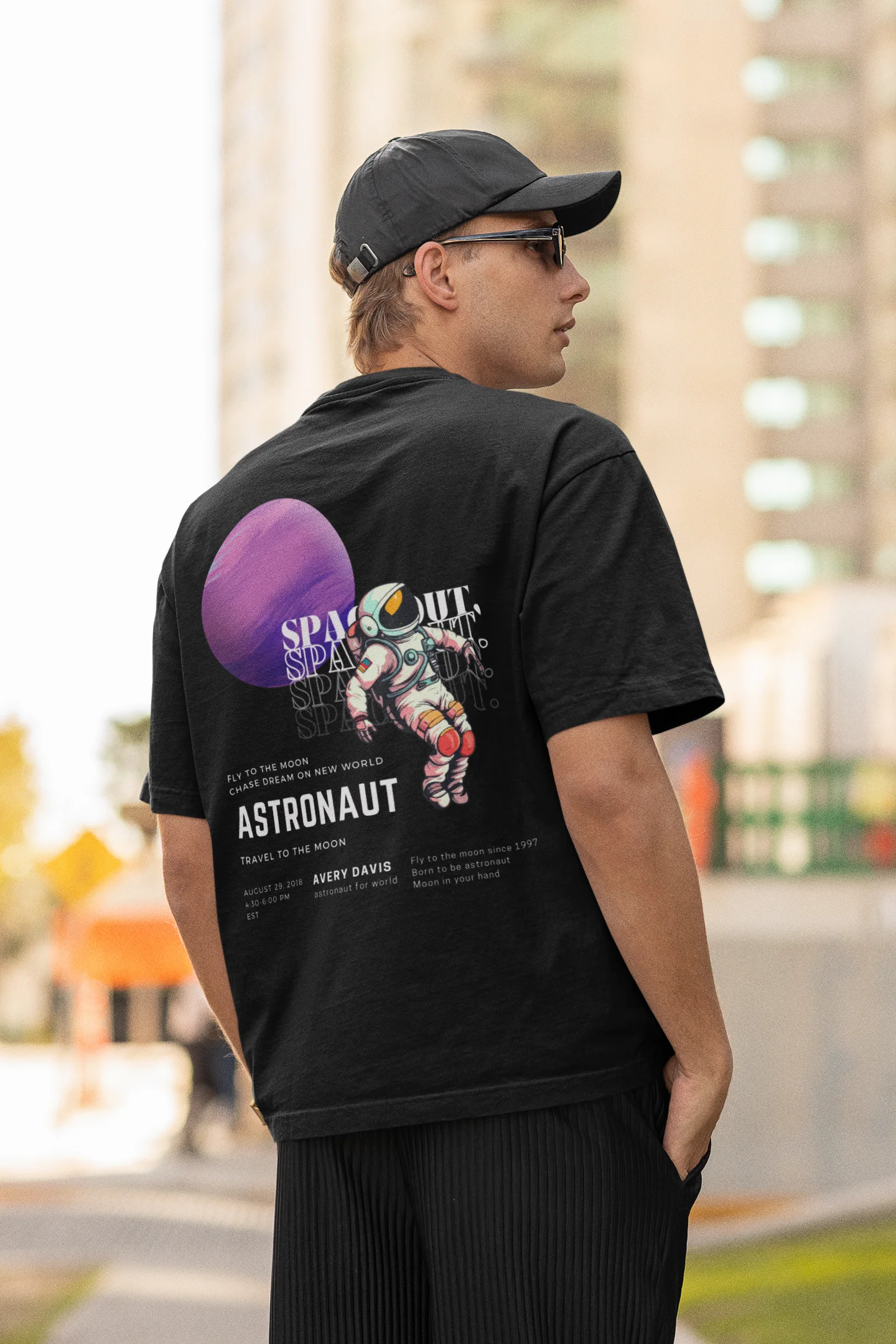 Back view of a male model wearing a black oversized t-shirt featuring a design inspired by the cosmos and galaxies "Fly Me to the Moon" and subtle hints of space exploration.