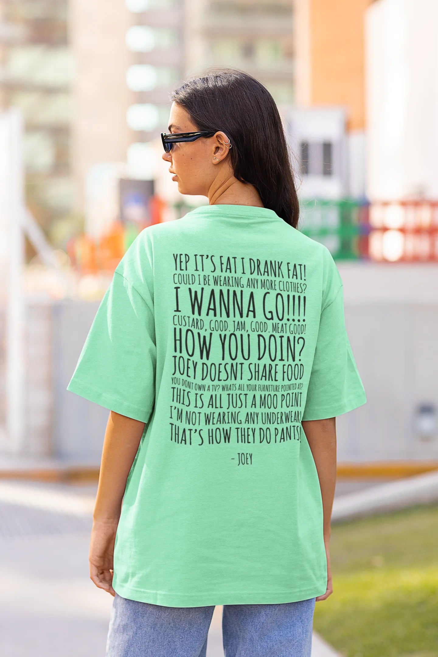 Back view of female model wearing a mint green oversized F.R.I.E.N.D.S. t-shirt featuring a design inspired by Joey Tribbiani's funny quotes and signature charm.