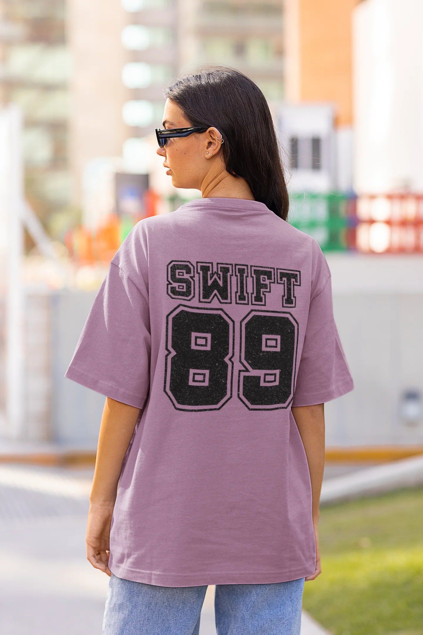 Back view of a woman wearing Dirty Purple coloured Oversize T-shirt featuring Taylor Swift 1989 design, Taylor's Version, and Eras Tour Merch