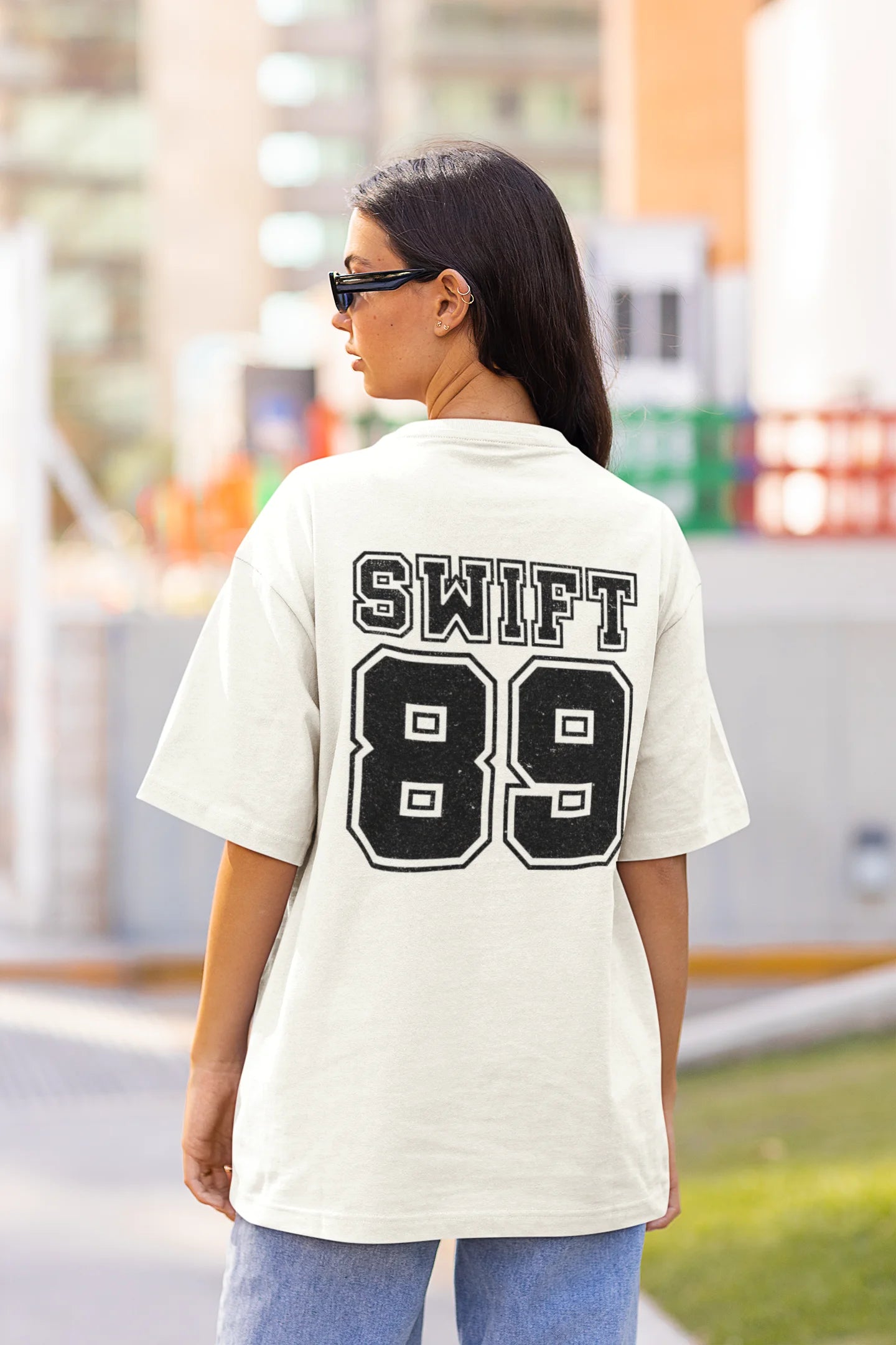 Back view of a woman wearing Off White coloured Oversize T-shirt featuring Taylor Swift 1989 design, Taylor's Version, and Eras Tour Merch