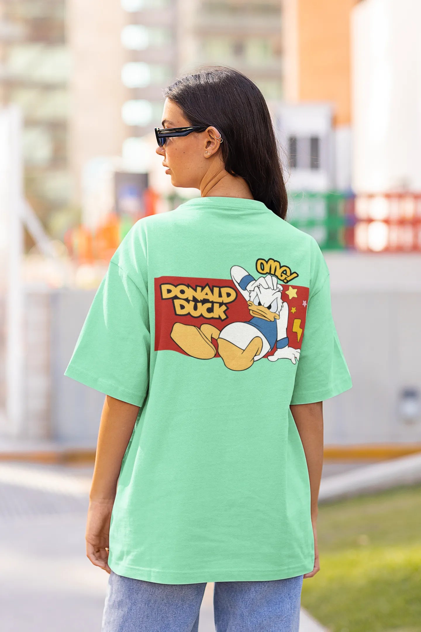 Back view of female model wearing mint green oversized Disney collection t-shirt featuring a classic Donald Duck design.