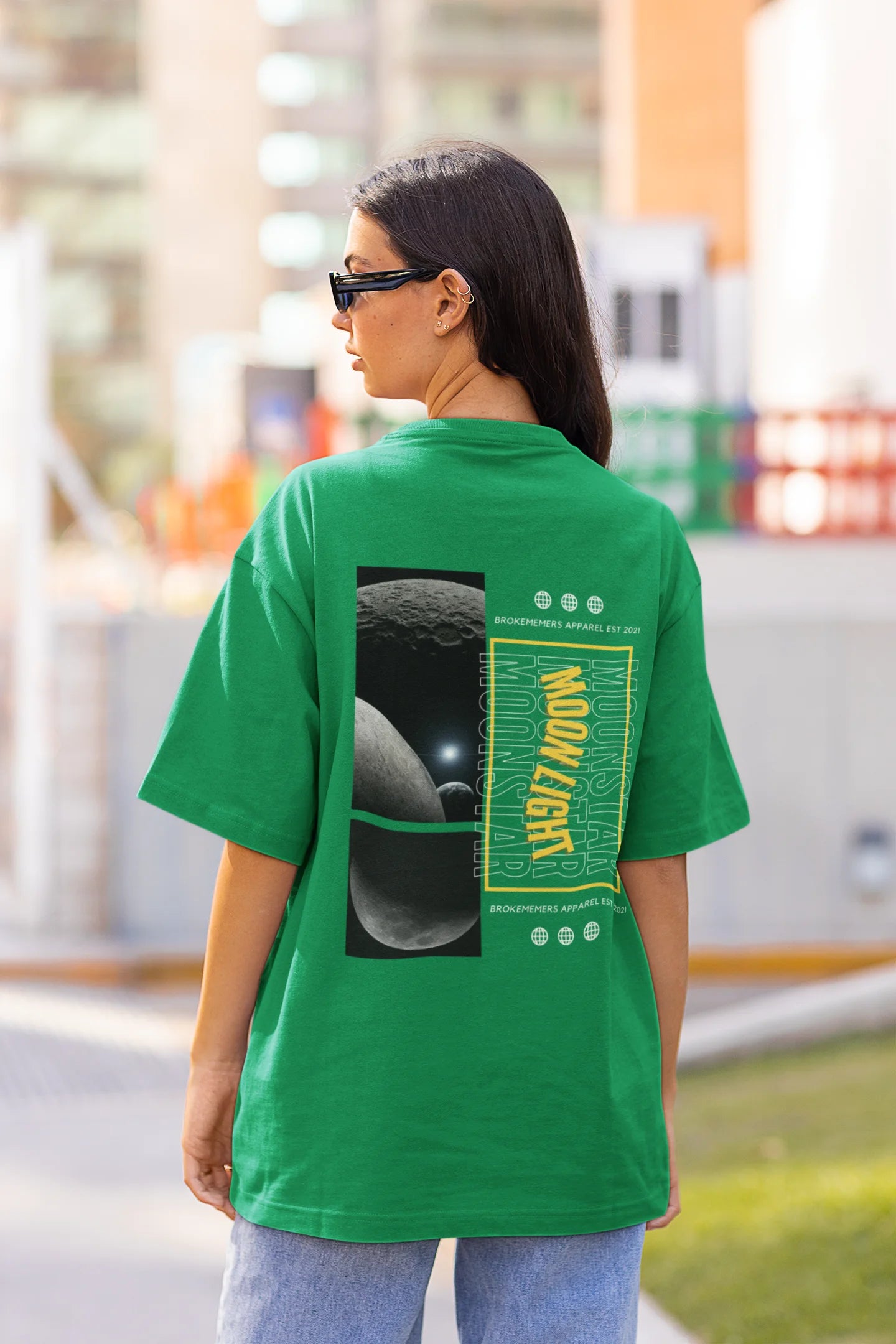 Back view of female model wearing a forest green oversized t-shirt featuring a captivating "moonlight" design with subtle elements of the Milky Way galaxy, planets, and the soft glow of the moon.