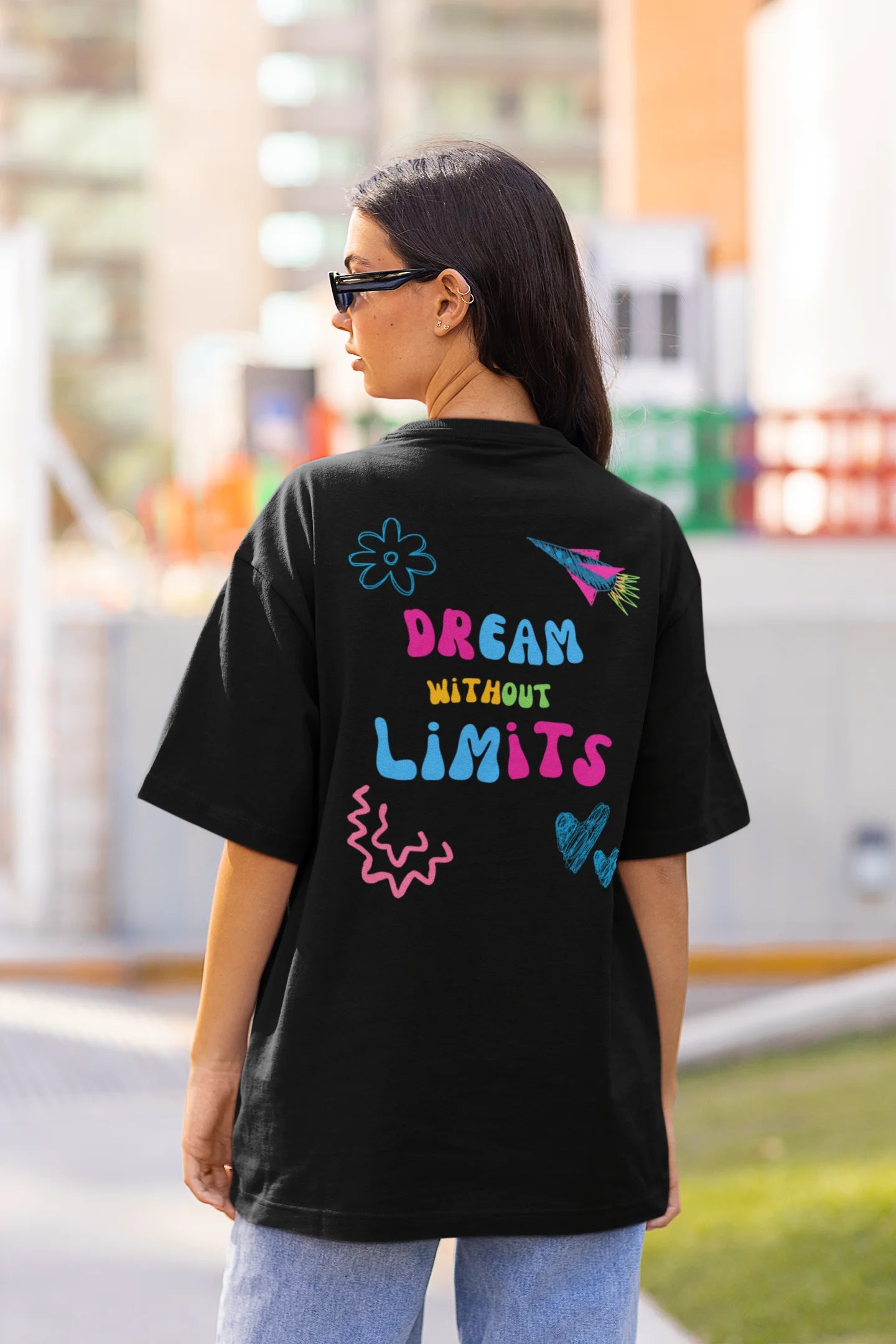 Back view of a female model wearing an black oversized t-shirt featuring colorful "Dream Without Limits" text, offering an inspiring and uplifting aesthetic.