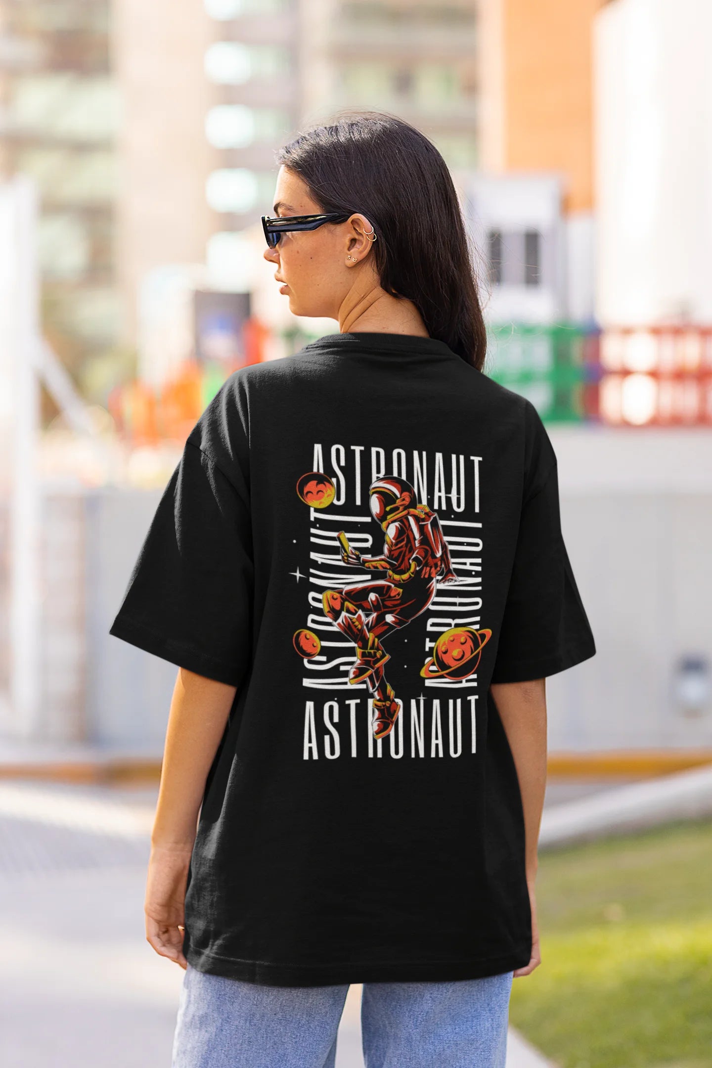 Back view of female model wearing a black oversized t-shirt featuring a captivating "celestial" design that incorporates subtle elements of the Milky Way galaxy, planets, and the wonders of space. Ideal for aspiring astronauts and space enthusiasts.