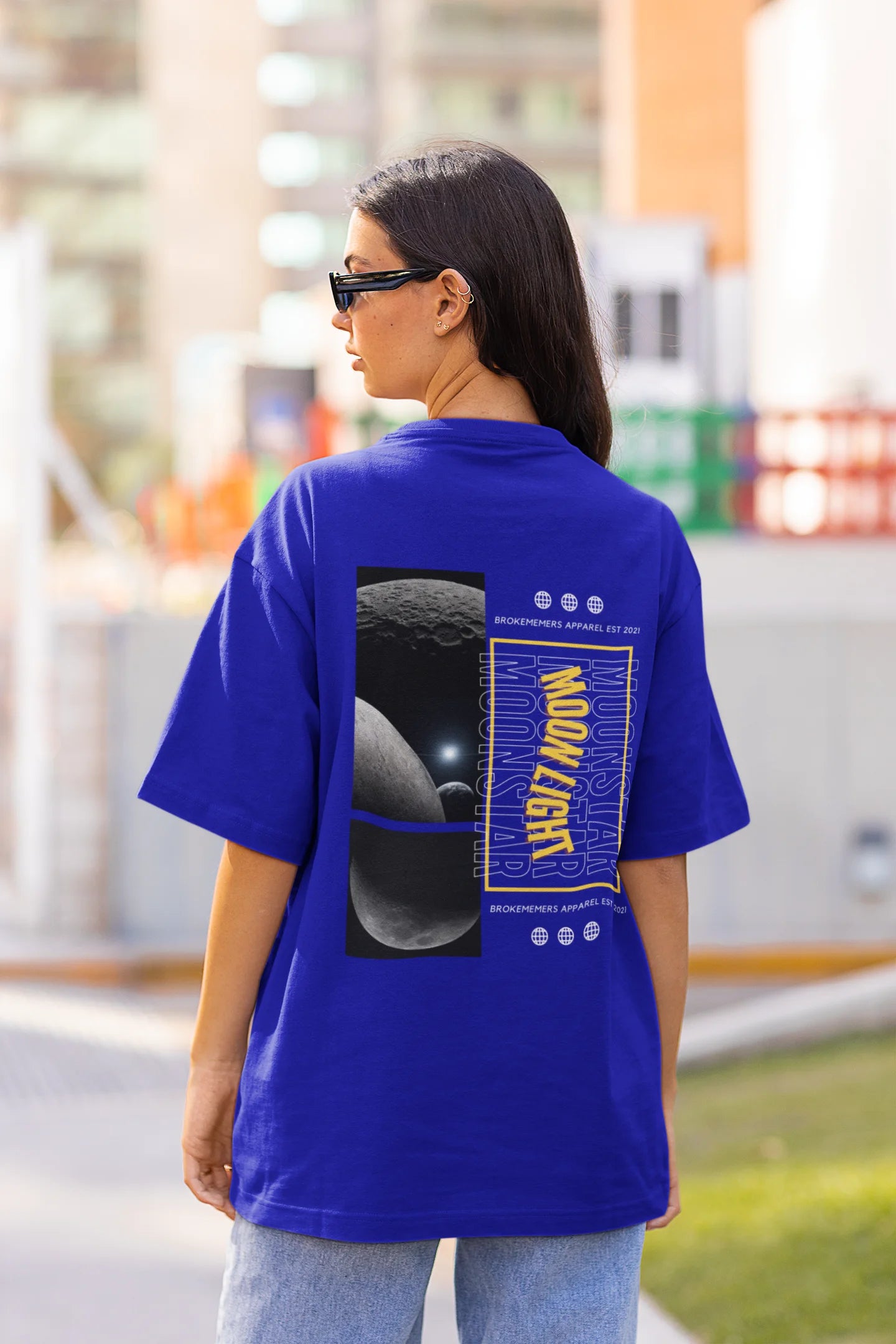 Back view of female model wearing a royal blue oversized t-shirt featuring a captivating "moonlight" design with subtle elements of the Milky Way galaxy, planets, and the soft glow of the moon.