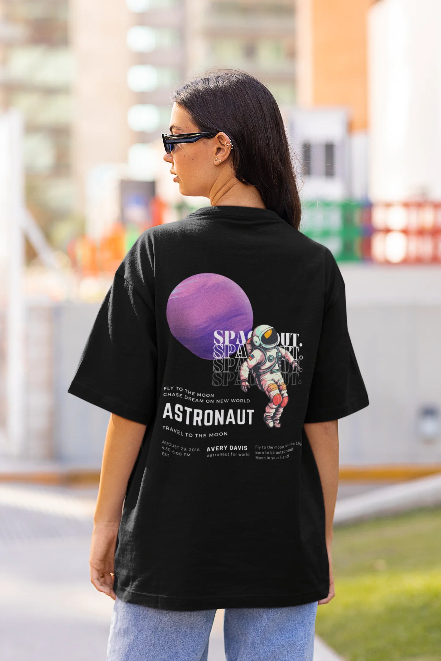 Back view of a female model wearing a black oversized t-shirt featuring a design inspired by the cosmos and galaxies "Fly Me to the Moon" and subtle hints of space exploration.