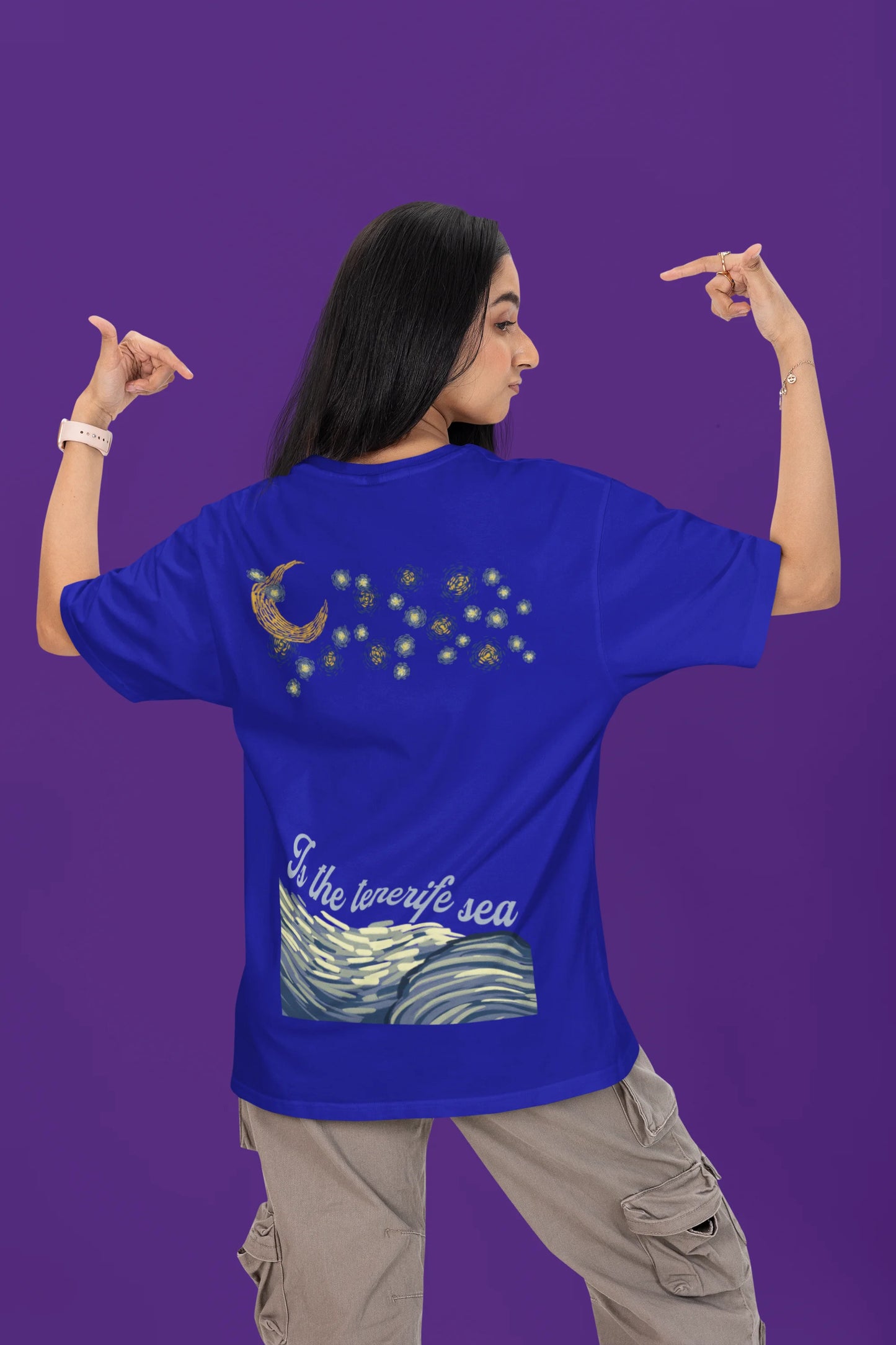 Back view of a female model wearing a royal blue oversized t-shirt featuring a beach at night with a starry sky above, inspired by Ed Sheeran's "Tenerife Sea."