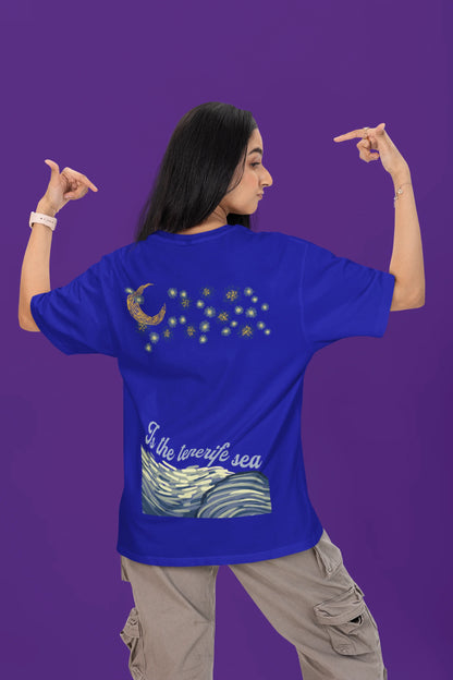 Back view of a female model wearing a royal blue oversized t-shirt featuring a beach at night with a starry sky above, inspired by Ed Sheeran's "Tenerife Sea."