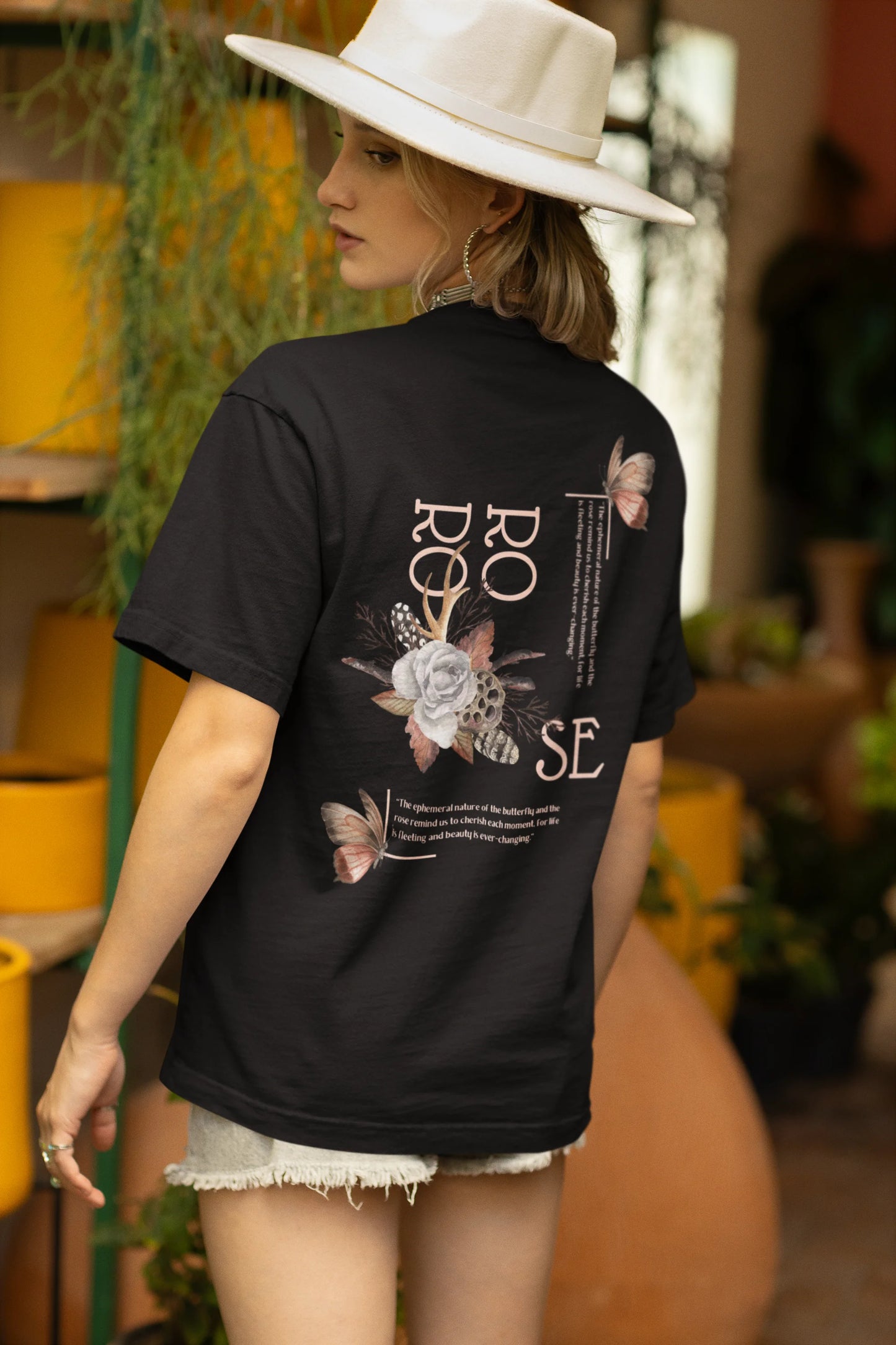 Back view of a female model wearing a black oversized t-shirt featuring a beautiful rose design with inspirational text, offering a calming and uplifting aesthetic.