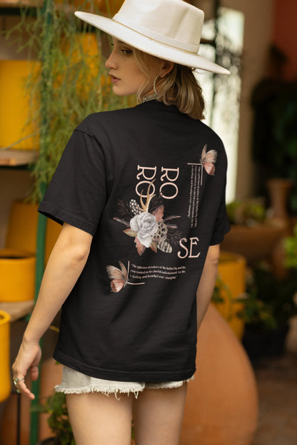 Back view of a female model wearing a black oversized t-shirt featuring a beautiful rose design with inspirational text, offering a calming and uplifting aesthetic.