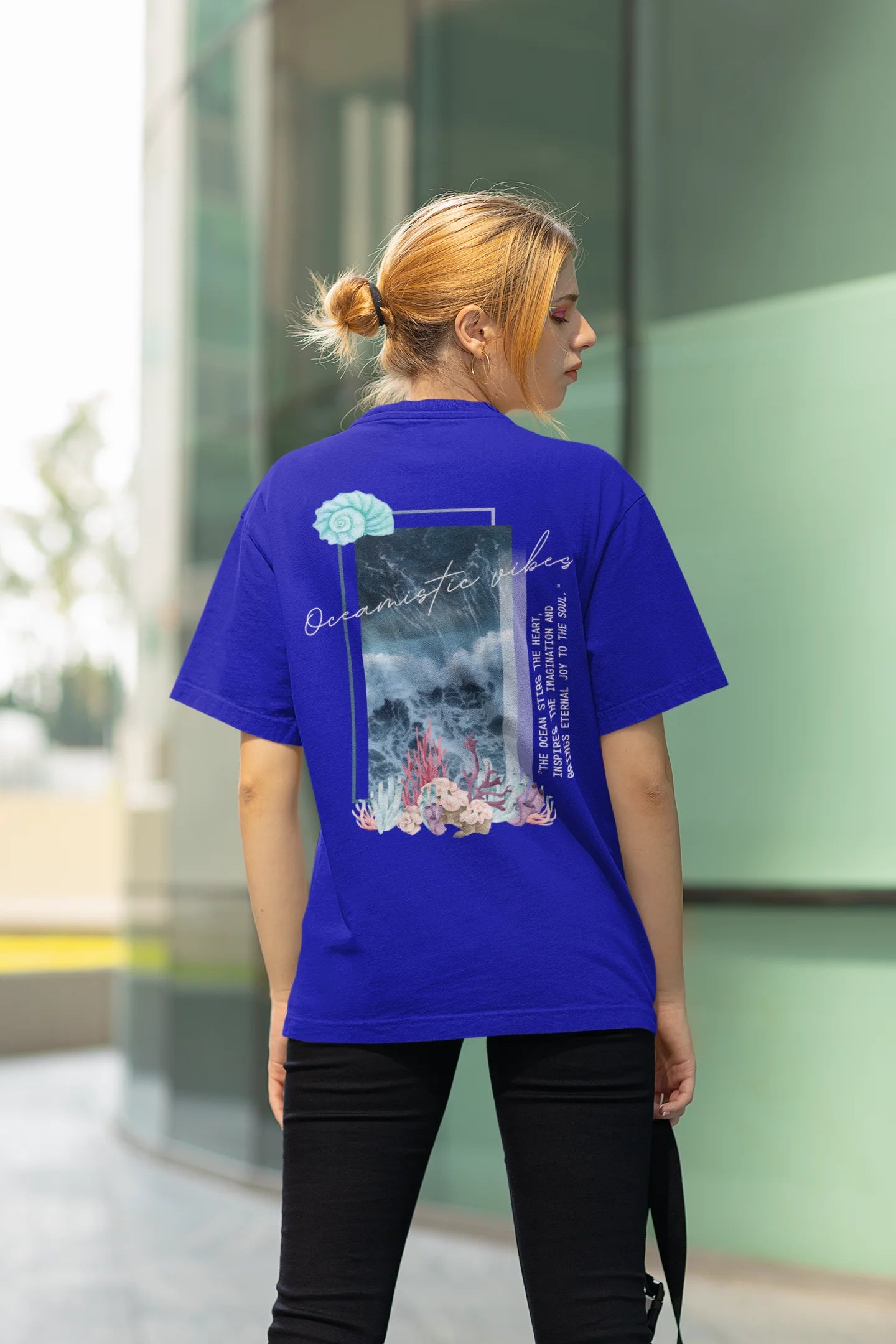 Back view of a female model wearing a royal blue Oversized t-shirt featuring a stunning design of corals and shells, evoking a serene underwater atmosphere.