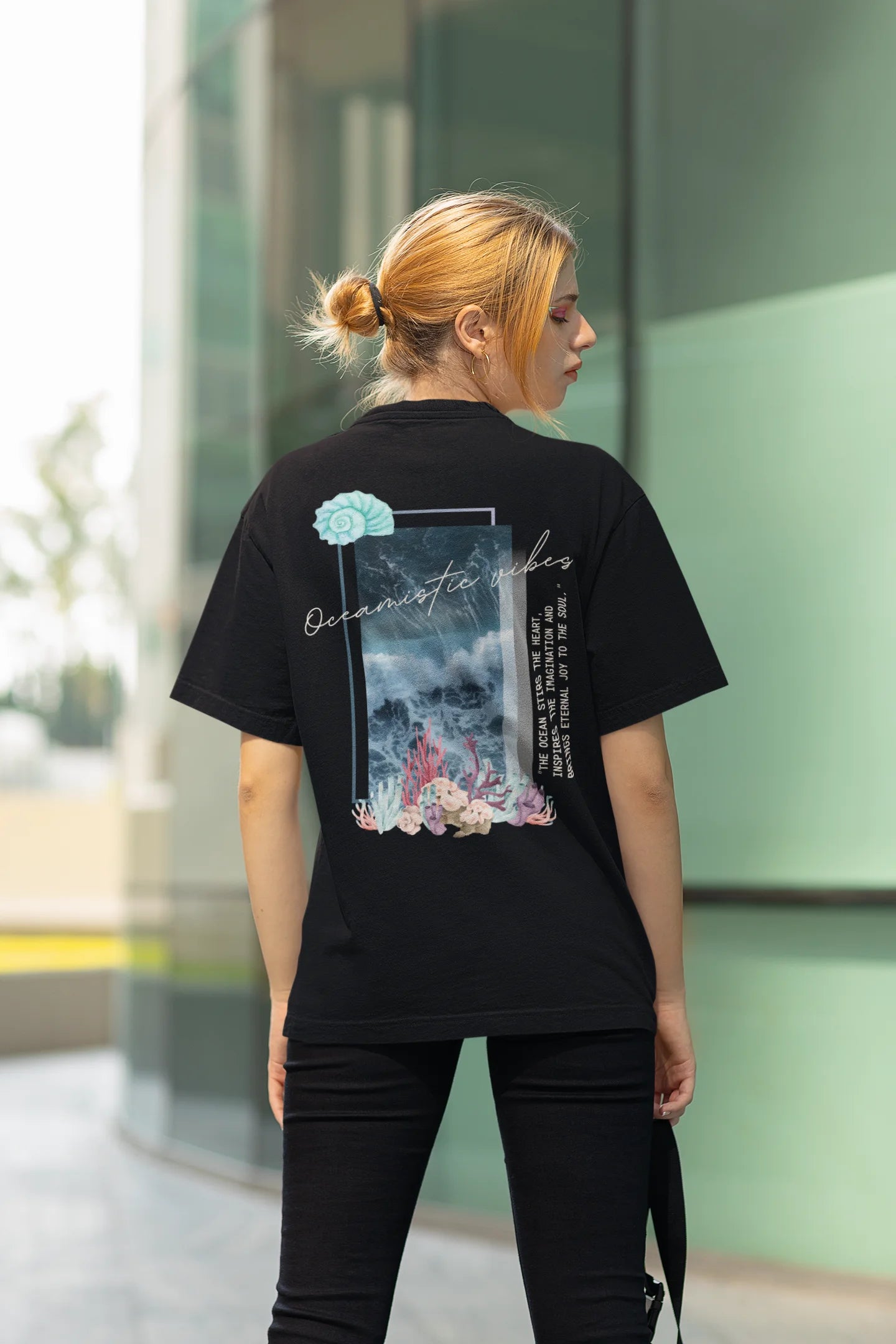 Back view of a female model wearing a black Oversized t-shirt featuring a stunning design of corals and shells, evoking a serene underwater atmosphere.