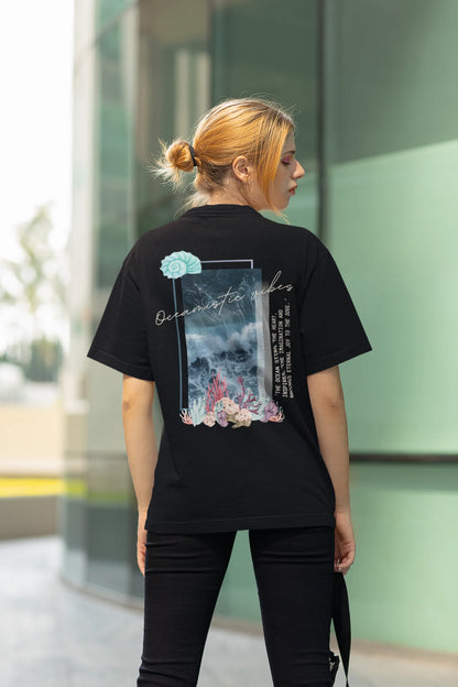 Back view of a female model wearing a black Oversized t-shirt featuring a stunning design of corals and shells, evoking a serene underwater atmosphere.