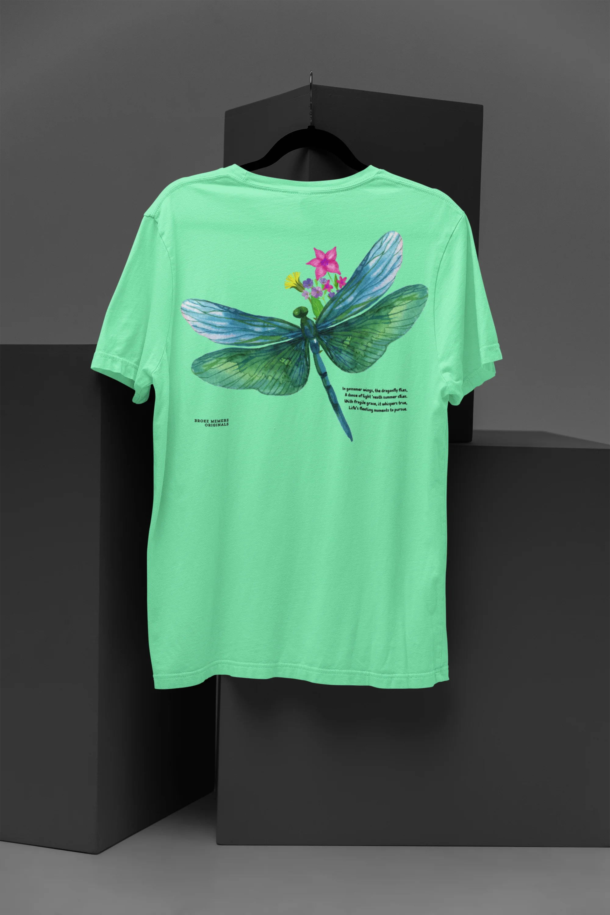 Back view of a mint green oversized t-shirt featuring a nature-inspired design with a blue dragonfly perched on flowers amidst green grass. Ideal for those who love springtime aesthetics and dragonfly imagery.