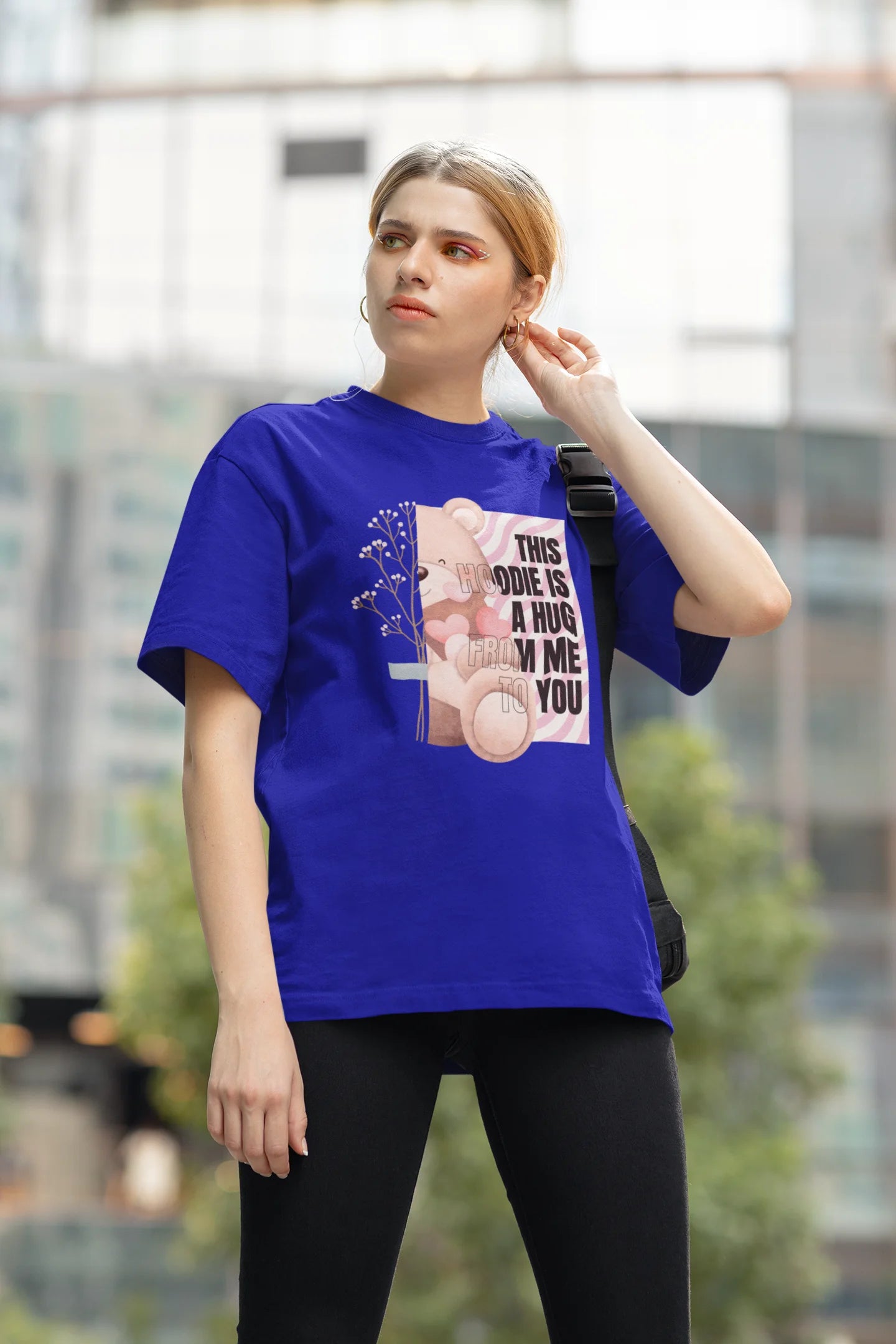 Second front view of a female model wearing an royal blue oversized t-shirt with a heartwarming design of a teddy bear offering a hug, offering a comforting and relaxing aesthetic.