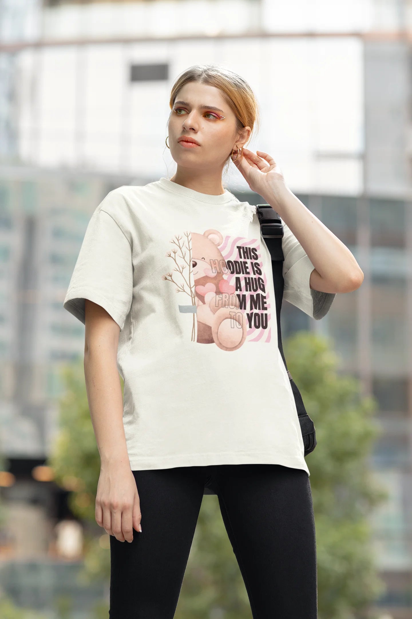 Third front view of a female model wearing an off-white oversized t-shirt with a heartwarming design of a teddy bear offering a hug, offering a comforting and relaxing aesthetic.