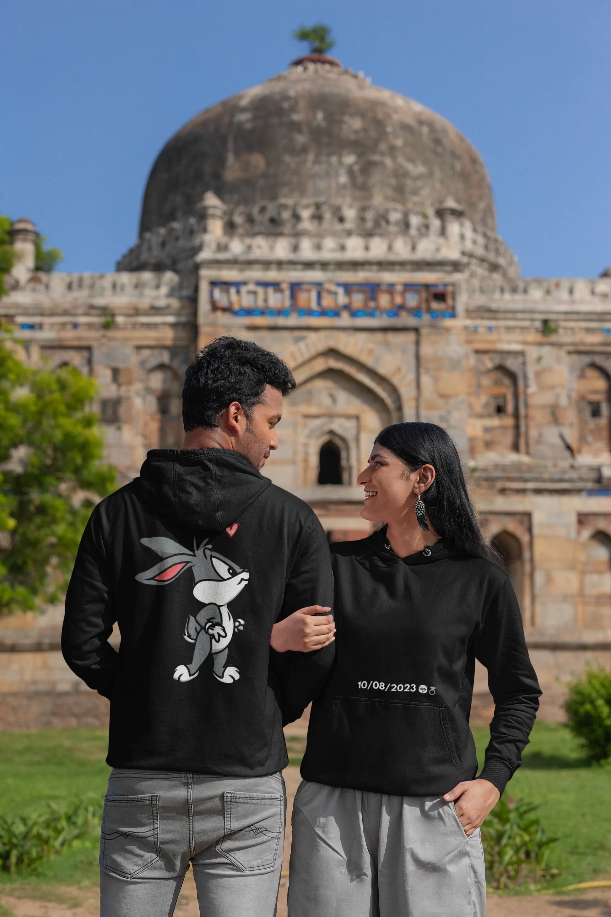 First back and front view of a couple wearing matching hoodies, one with a Bugs Bunny design and the other with a Lola Bunny design.