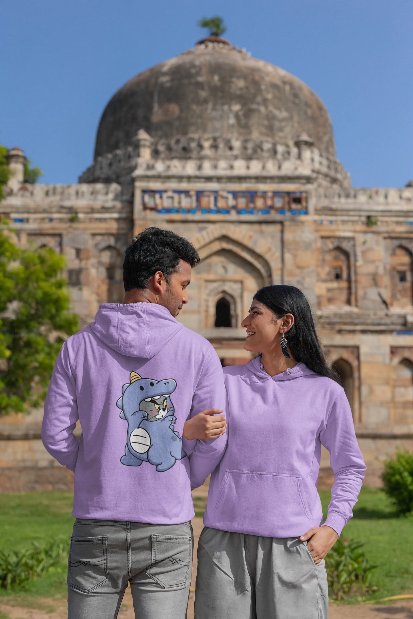 First back and front view of a couple wearing matching lavender hoodies, one with Tom the cat and the other with Jerry the mouse, both dressed in dinosaur costumes.