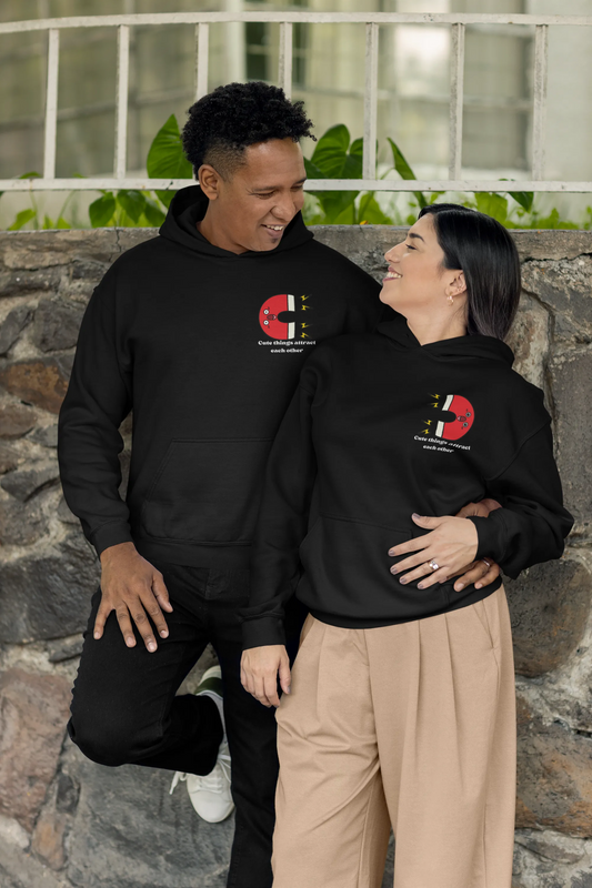 First front view of a couple wearing matching hoodies with a design of two animated magnets attracting each other, and the text "Cute Things Attract".