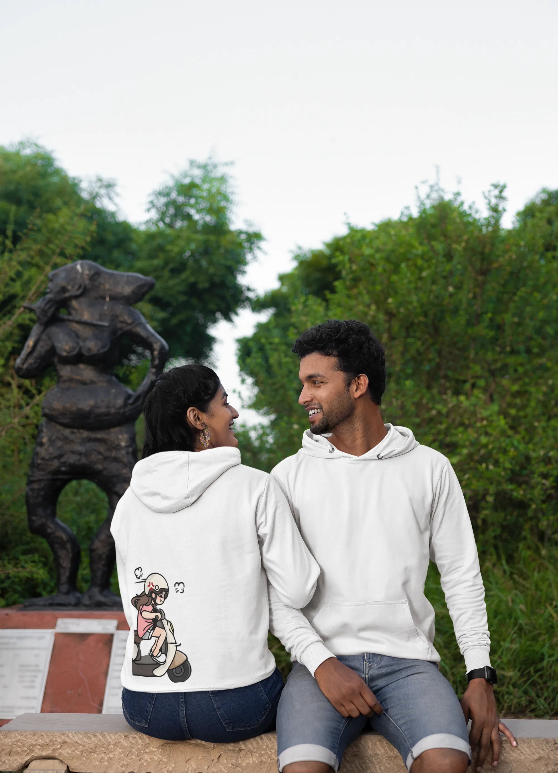2nd back and front view of a couple wearing matching hoodies with a split design. The left side shows a guy relaxing in the backseat of a scooter, while the right side shows his girlfriend driving off.