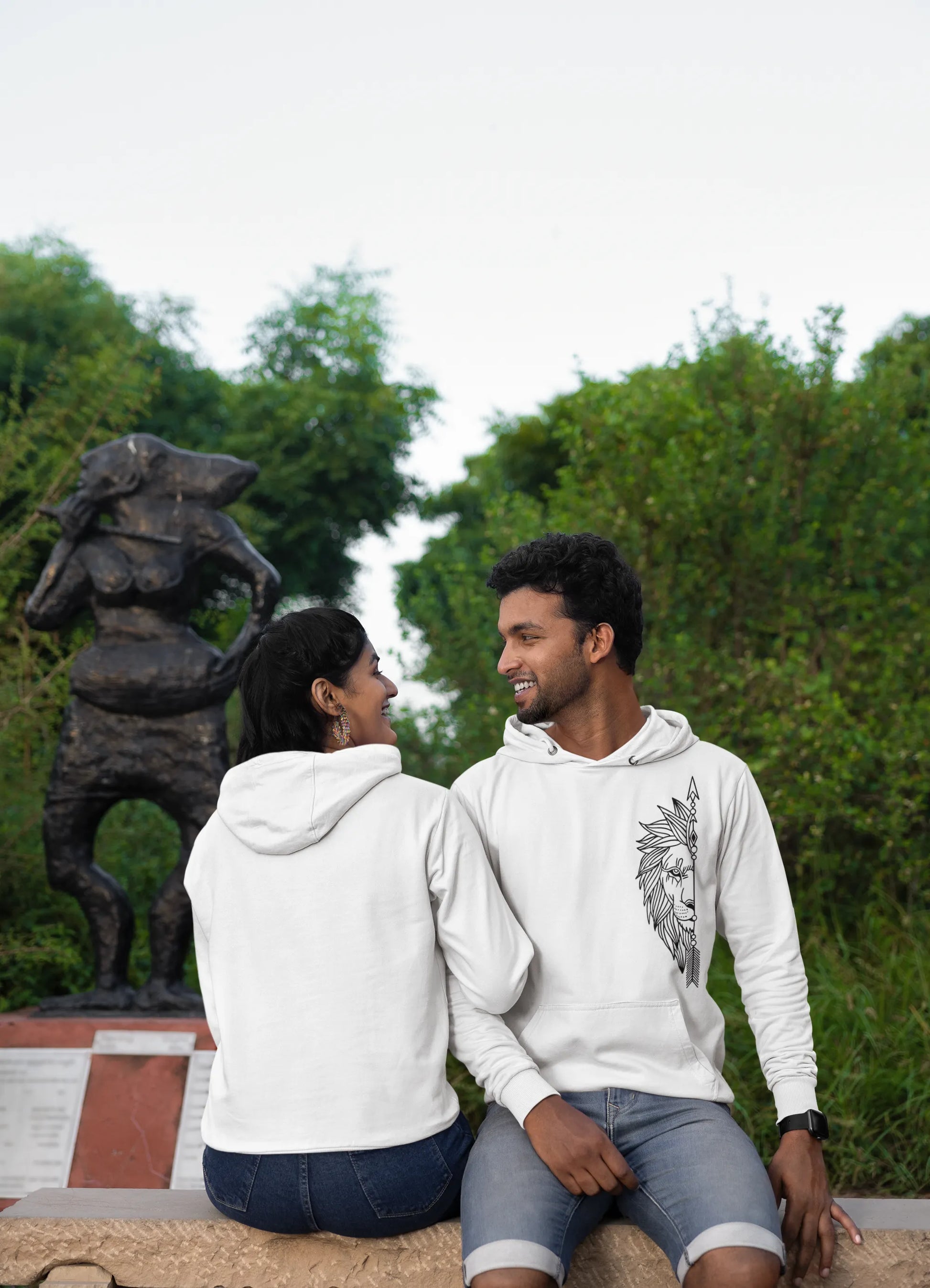First front and back view of a couple wearing matching hoodies, one with a lion outline and the other with a lioness outline.