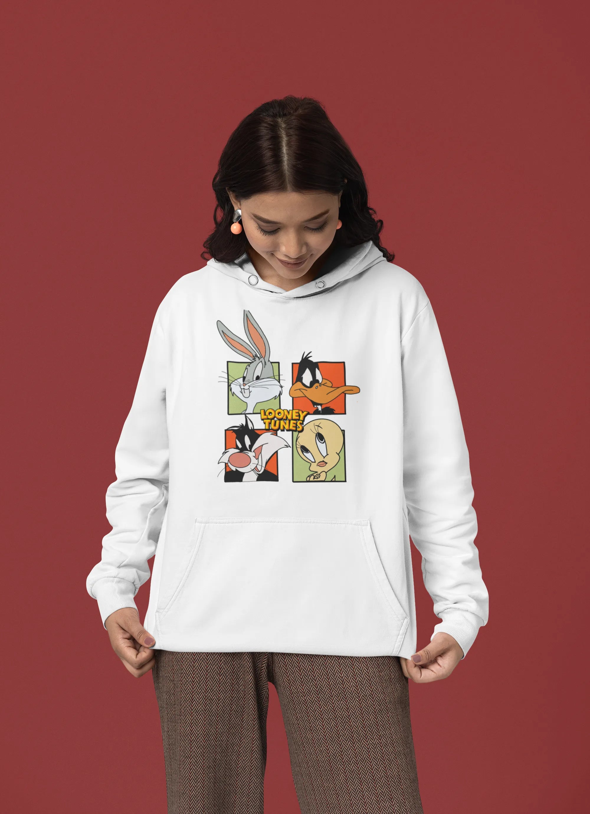 Third image of a female model wearing a white hoodie with a large Looney Tunes design. The illustration features portraits of several iconic Looney Tunes characters.