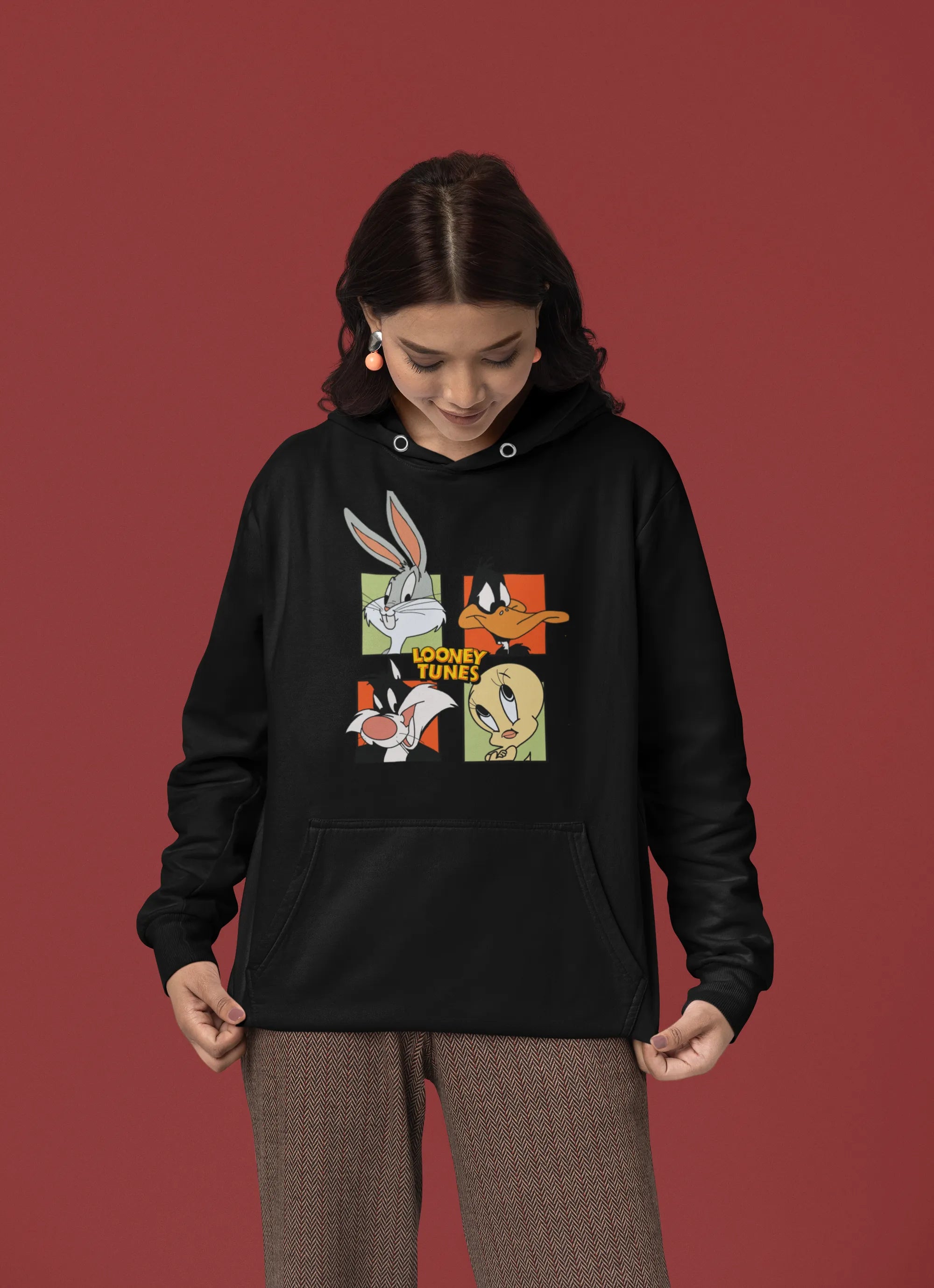 Fourth image of a female model wearing a black hoodie with a large Looney Tunes design. The illustration features portraits of several iconic Looney Tunes characters.