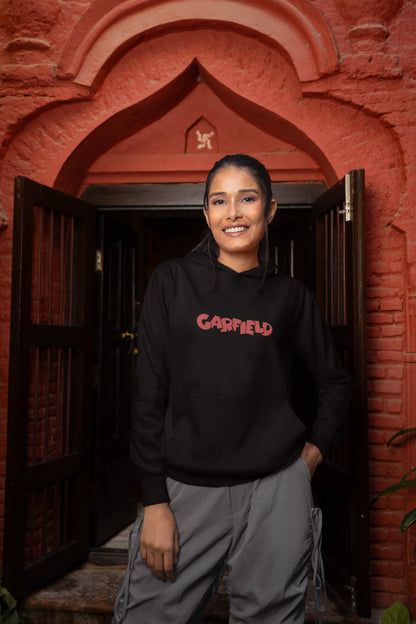 Second front view of a female model wearing a black hoodie with a large Garfield design. The illustration shows Garfield standing out of bed, yawning and stretching, still wearing his nightcap and pajamas.