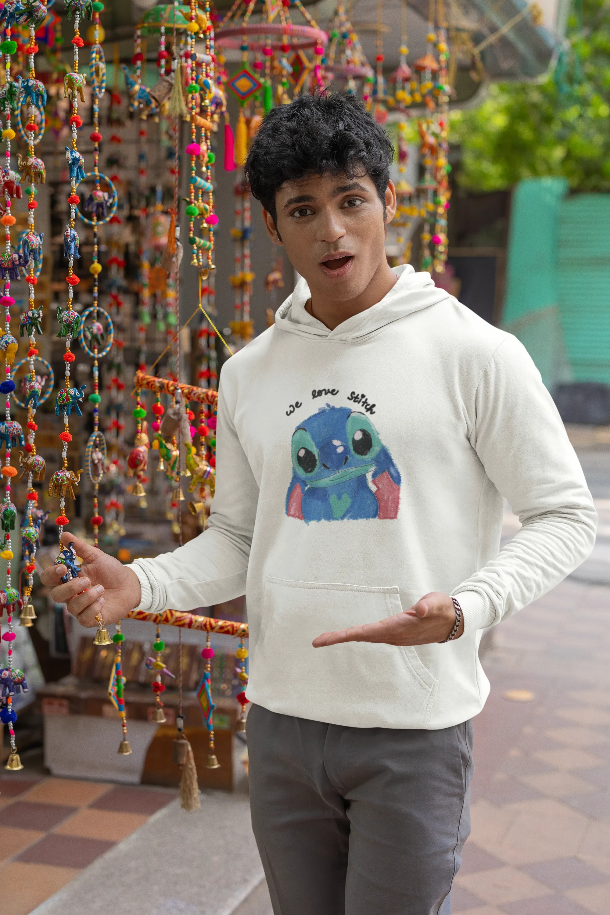 First front view of a male model wearing a white hoodie with a large Stitch design. The illustration shows Stitch smiling and waving.