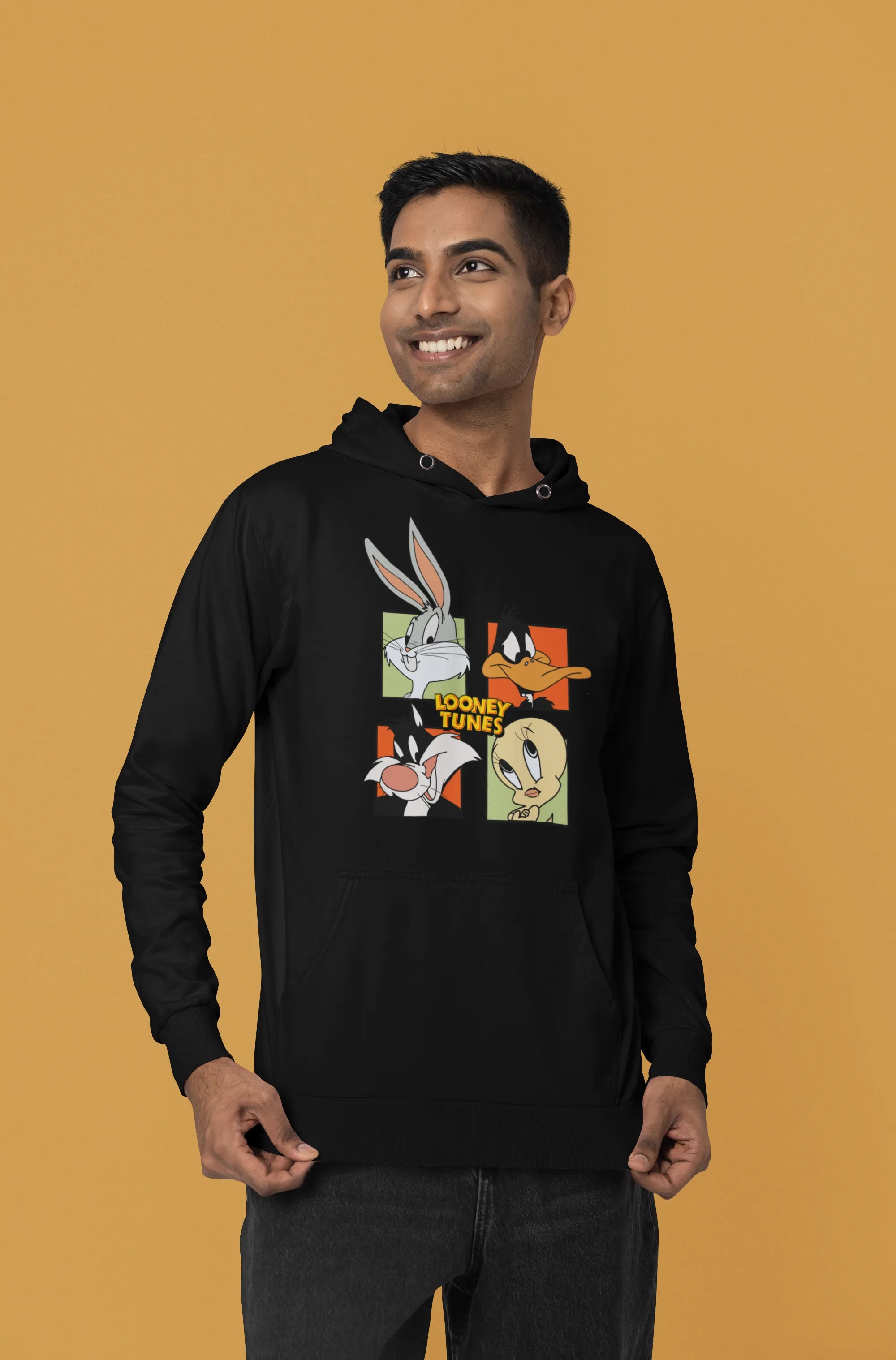 First image of a male model wearing a black hoodie with a large Looney Tunes design. The illustration features portraits of several iconic Looney Tunes characters.