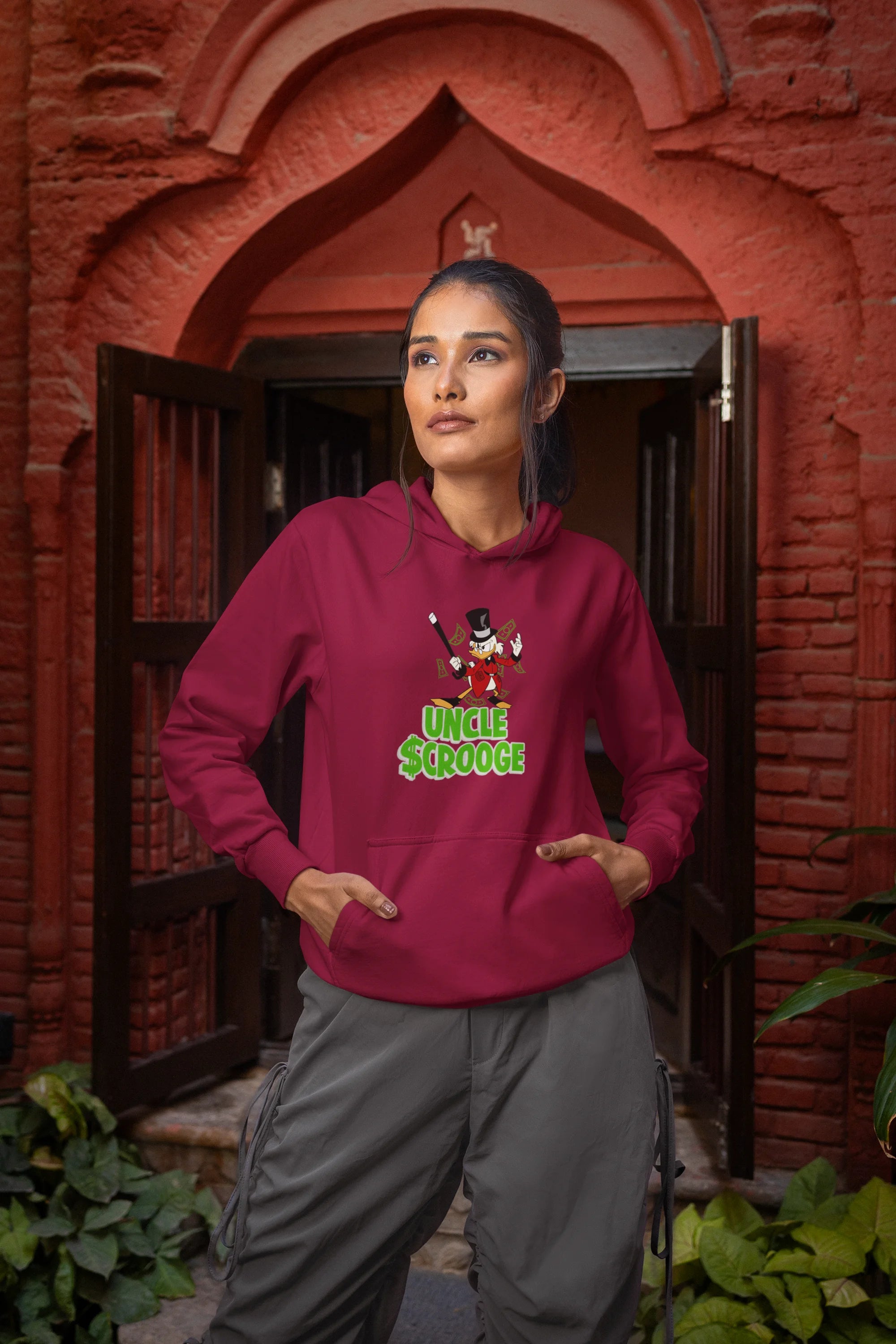 Front view of a female model wearing a maroon hoodie with a Disney Uncle Scrooge design, showing dollar bills raining down on him.