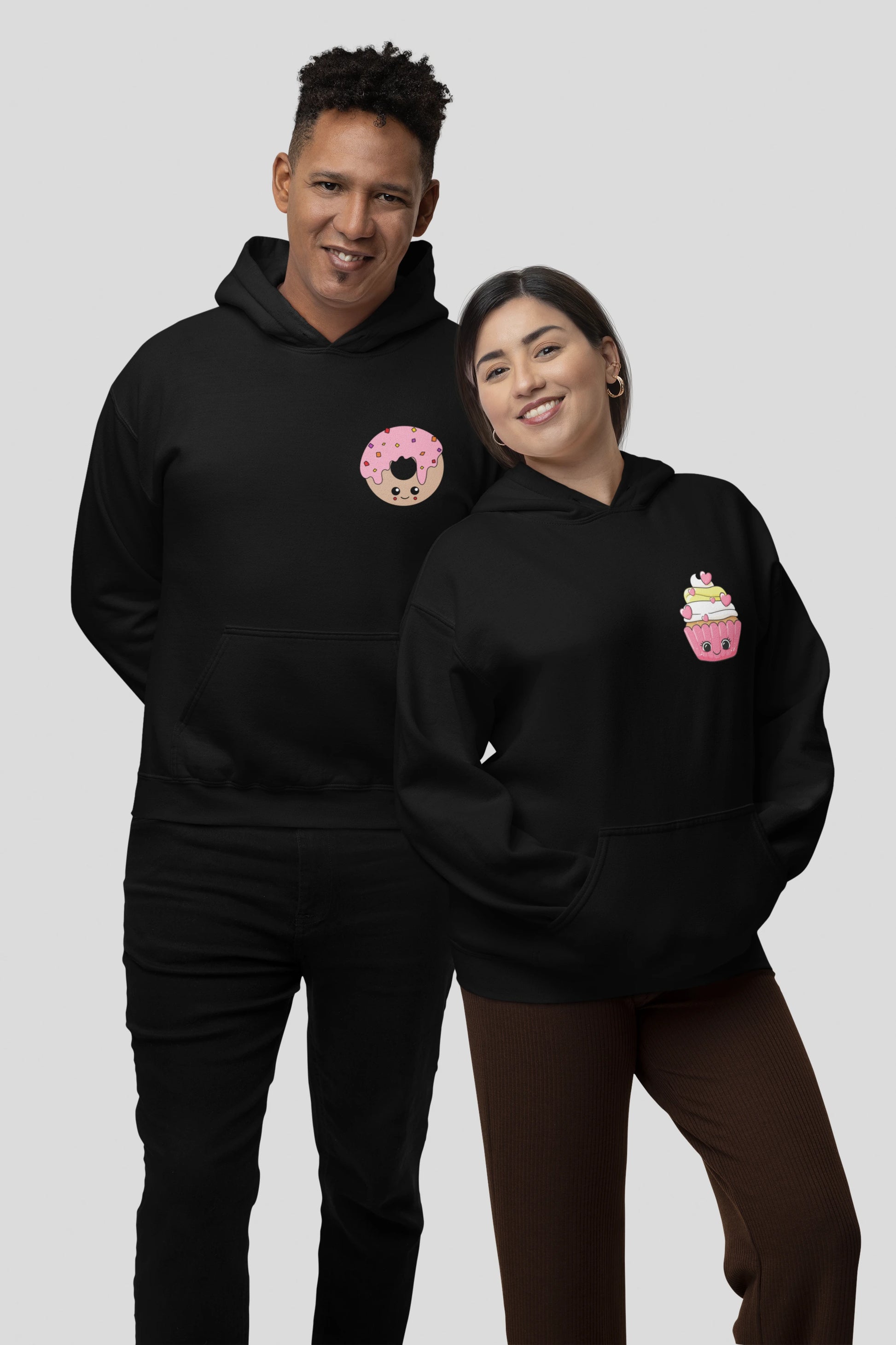 3rd front view of a couple wearing matching black hoodies, one with a animated donut and the other with a cupcake.