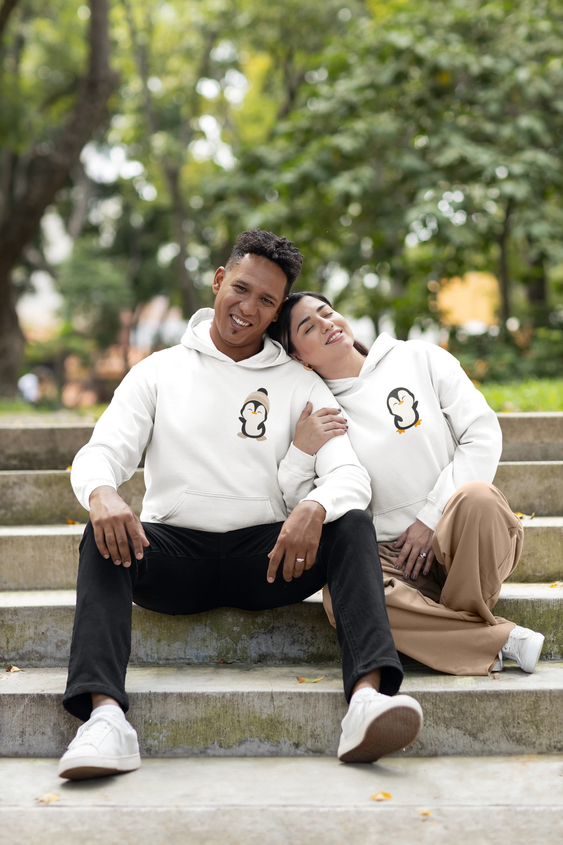First front view of a couple wearing matching cream hoodies with a design of two penguins wearing woolen hats.