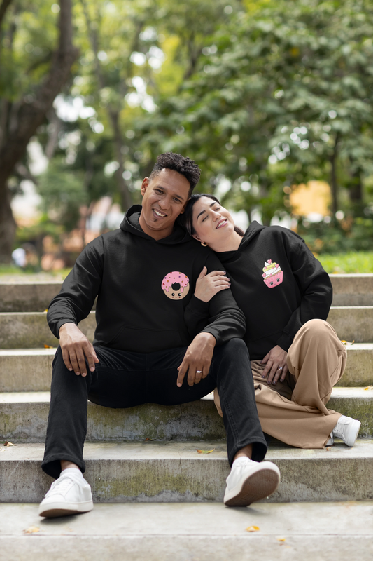 First front view of a couple wearing matching black hoodies, one with a animated donut and the other with a cupcake.