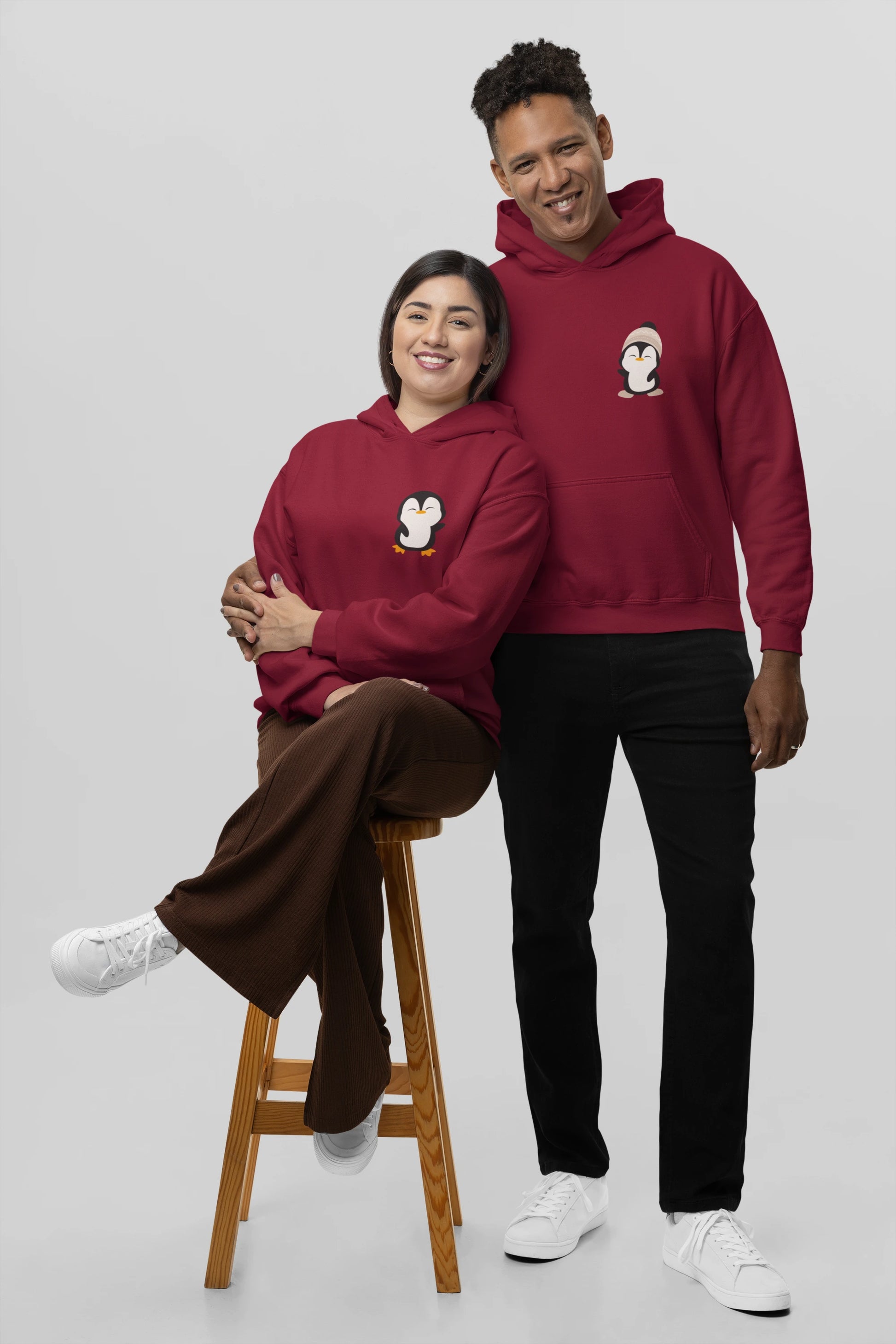 3rd front view of a couple wearing matching cream hoodies with a design of two penguins wearing woolen hats.