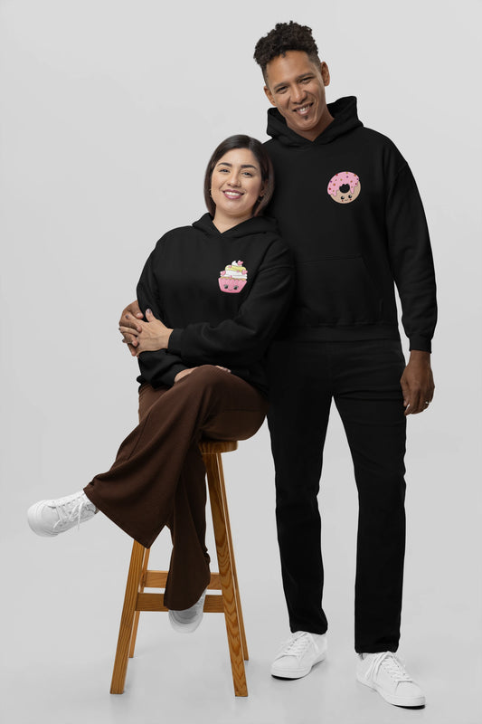 2nd front view of a couple wearing matching black hoodies, one with a animated donut and the other with a cupcake.