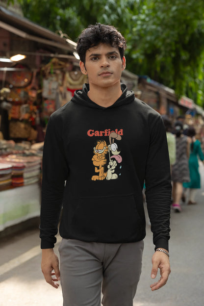 Fourth image of a male model wearing a black hoodie with a Garfield illustration showing the cat standing back to back with Odie, surrounded by a playful cartoon border.