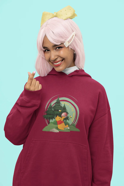 Close up front view of a female model wearing a maroon hoodie with a Winnie the Pooh design, showing the Disney bear eating honey from a jar in a forest.