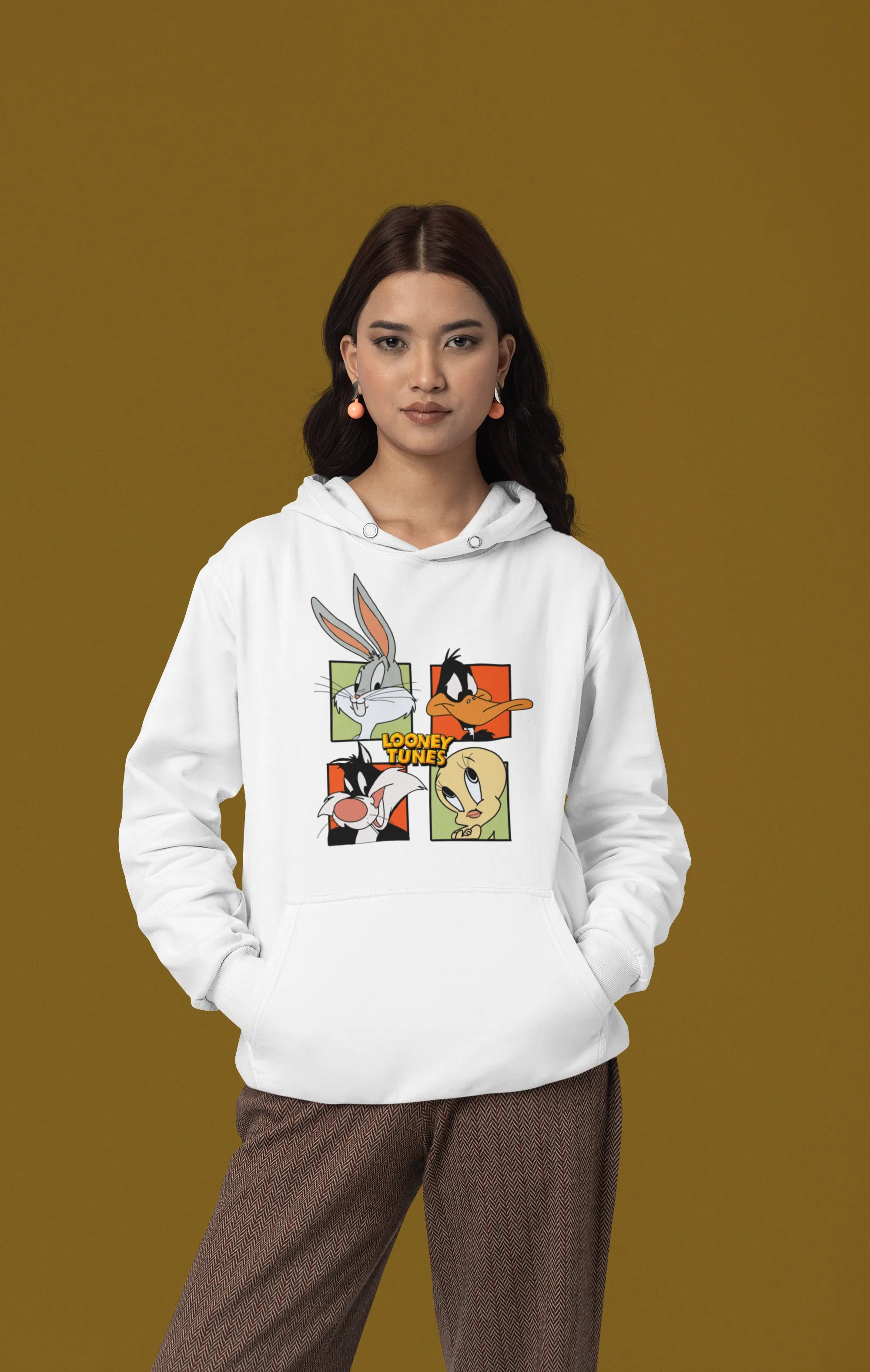 First image of a female model wearing a white hoodie with a large Looney Tunes design. The illustration features portraits of several iconic Looney Tunes characters.