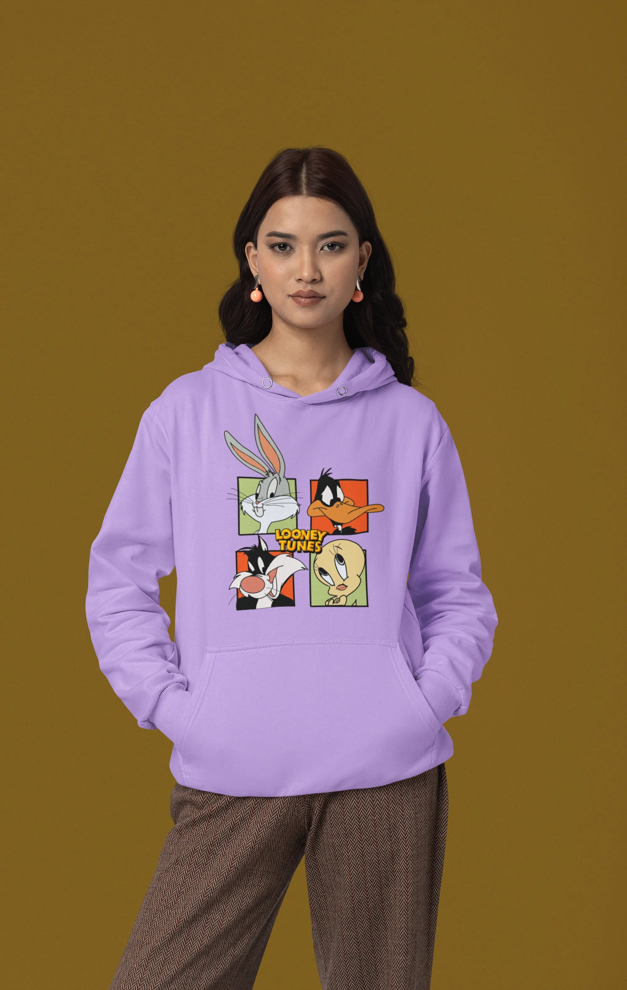 First image of a female model wearing a lavender hoodie with a large Looney Tunes design. The illustration features portraits of several iconic Looney Tunes characters.