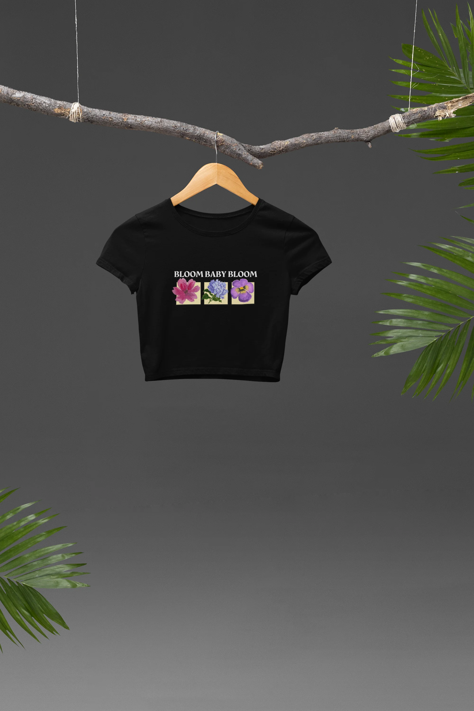 Front view of a black crop top with a floral "bloom baby bloom" design, exuding a cool and confident vibe.