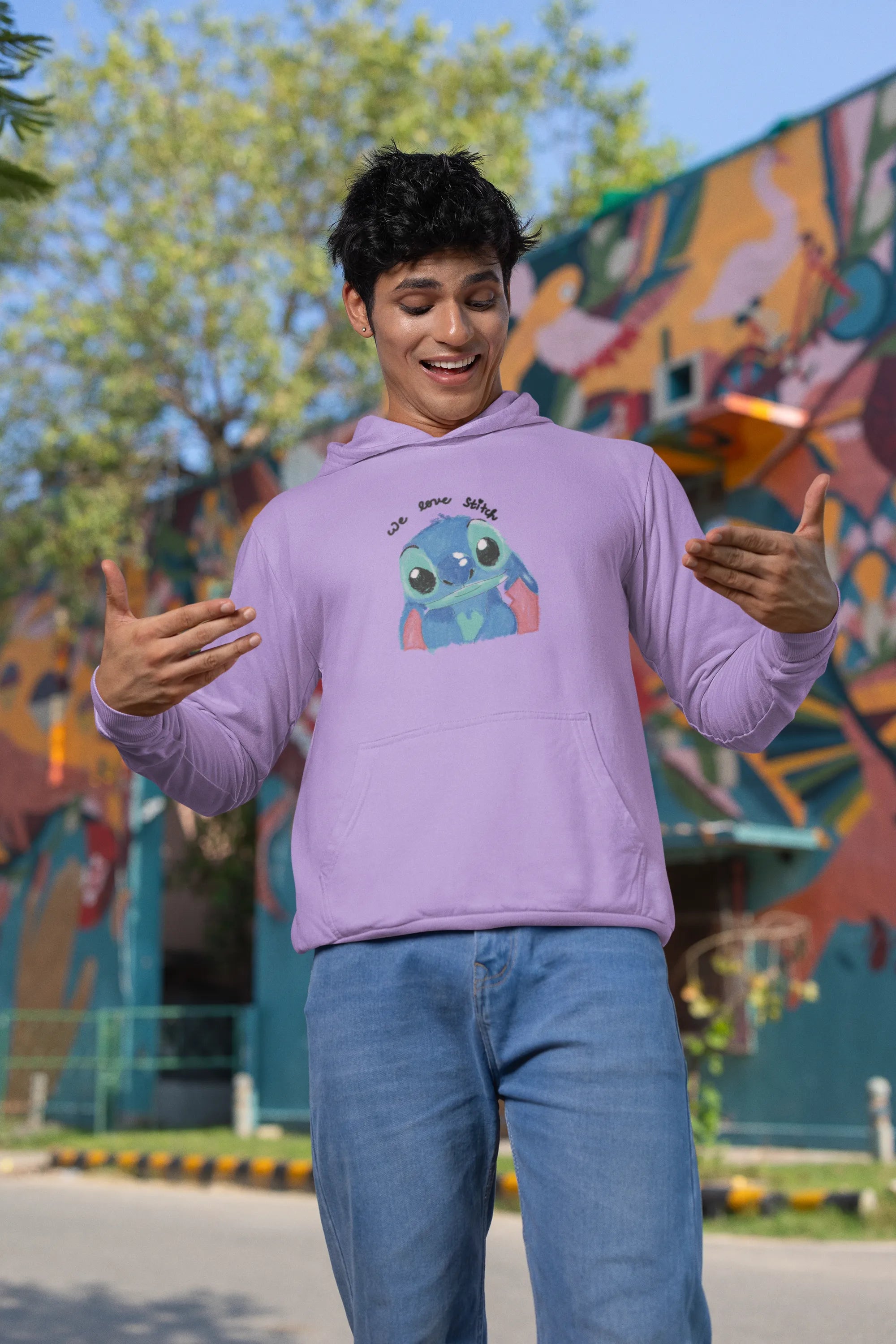 Second front view of a male model wearing a lavender hoodie with a large Stitch design. The illustration shows Stitch smiling and waving.